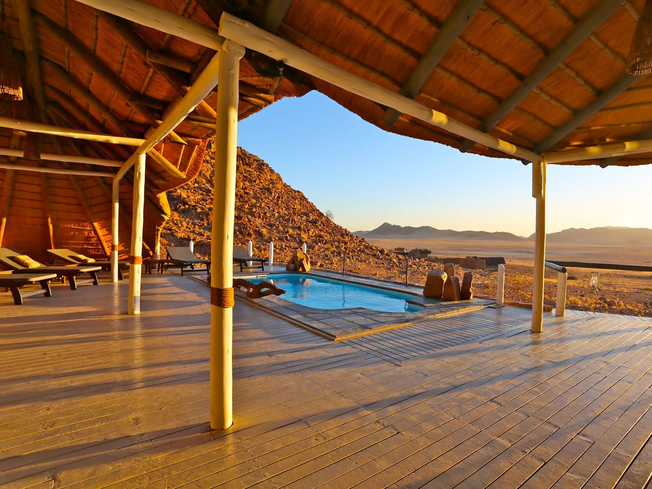Lodge-Terrasse mit Pool und Panoramablick auf die Felsenlandschaft des Erongo-Gebirges in Namibia bei Sonnenuntergang.