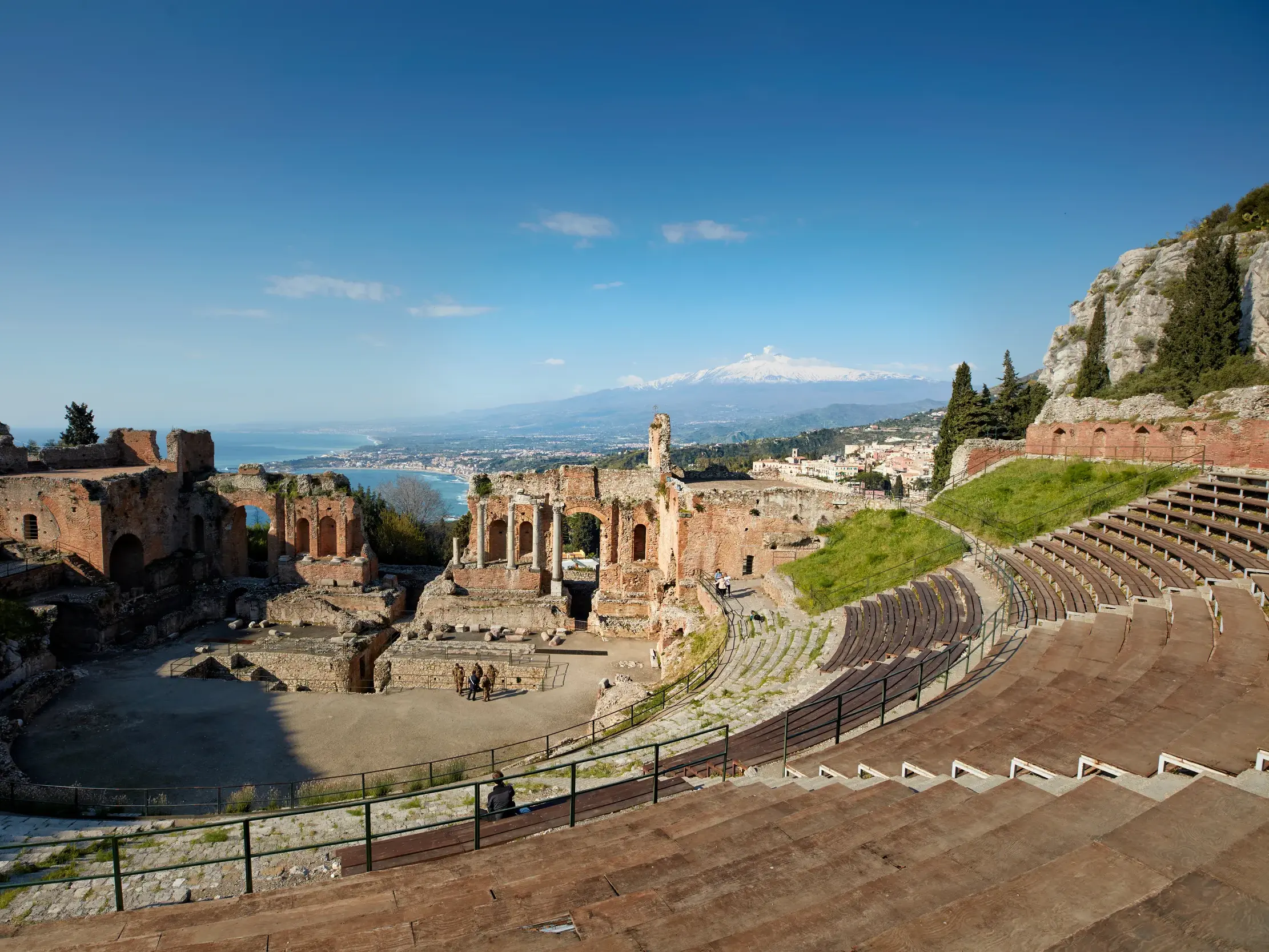 Panoramablick von den Rängen des antiken Theaters in Taormina auf die Bühne, das Meer und den schneebedeckten Vulkan Ätna.