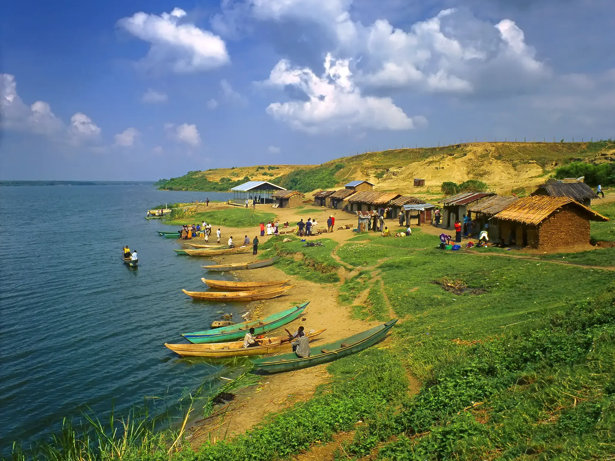 Lebhaftes Fischerdorf in Uganda mit Lehmhütten und Holzkanus am Ufer des Mutanda-Sees unter blauem Himmel.