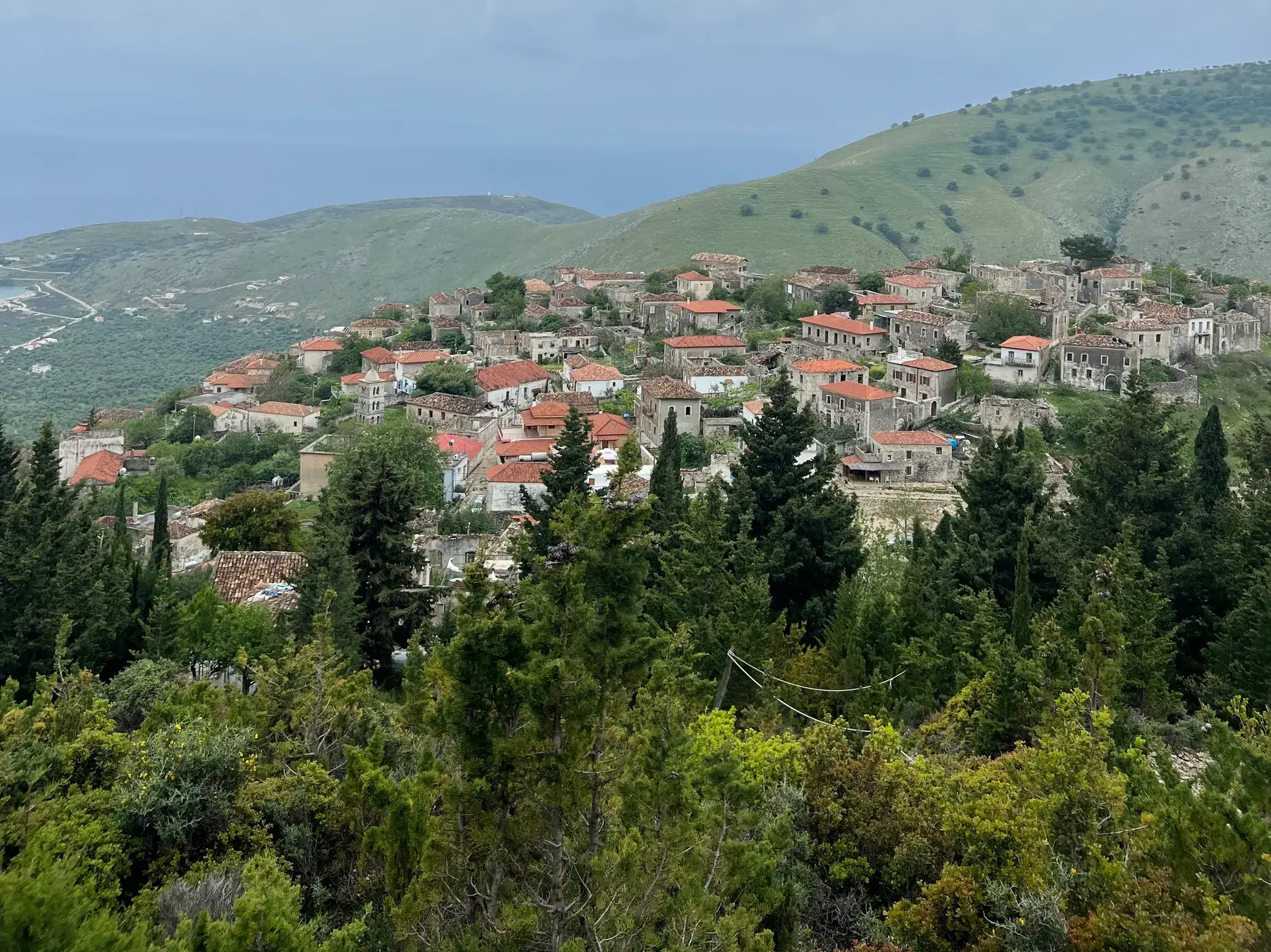 Blick auf die alten Steinhäuser des Bergdorfs Himare, das an einem grünen Hang an der albanischen Riviera liegt.