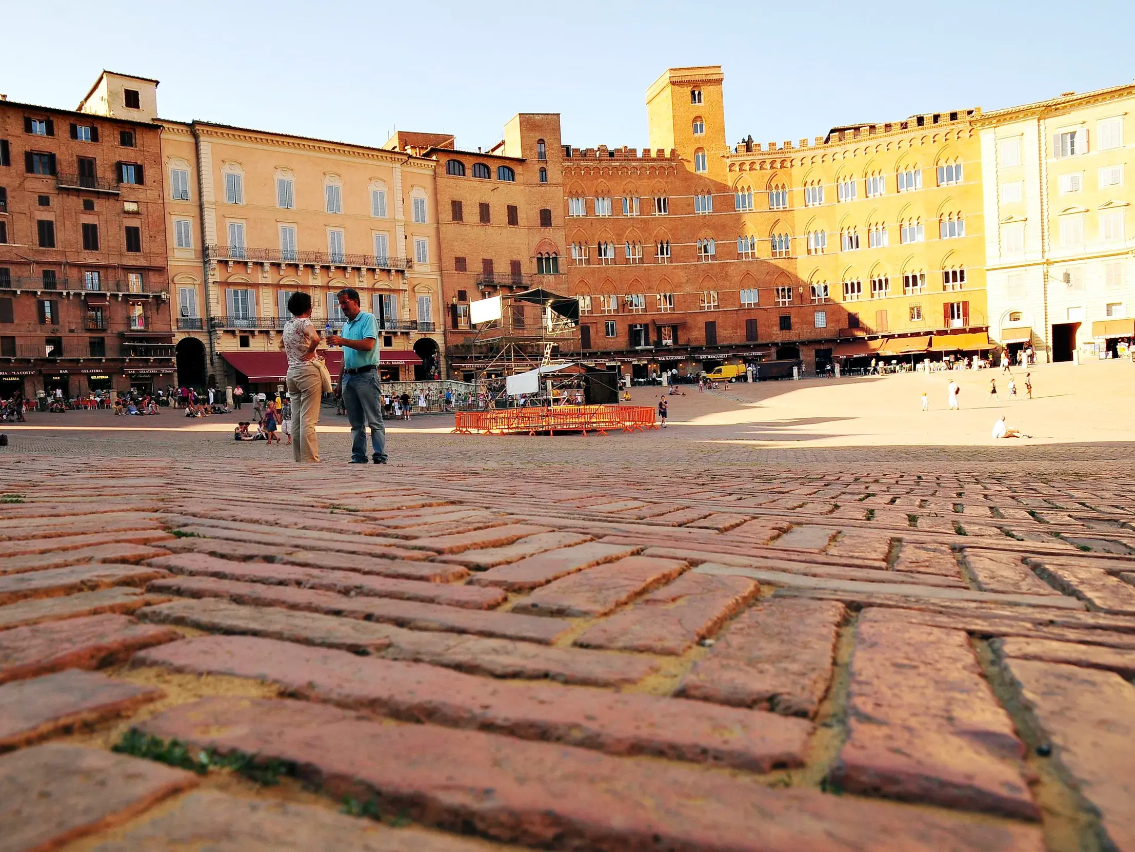 Wanderer genießen die Abendsonne auf dem weiten, ziegelroten Piazza del Campo in Siena, umgeben von historischen Palästen.