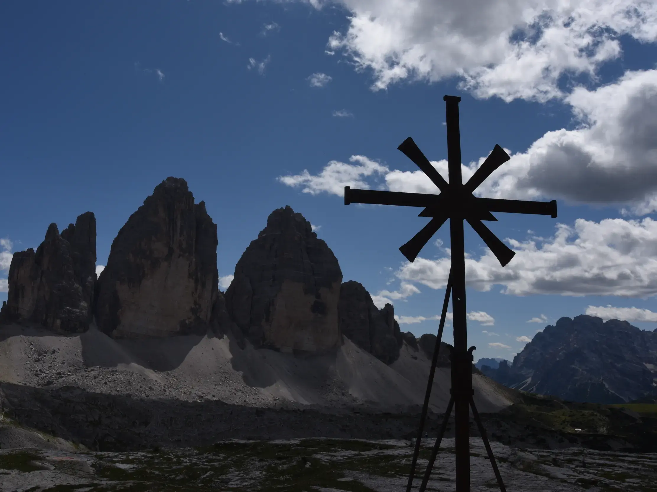 Silhouette eines sternförmigen Mahnmals vor dem Felsmassiv der Drei Zinnen im UNESCO Welterbe Dolomiten bei blauem Himmel.