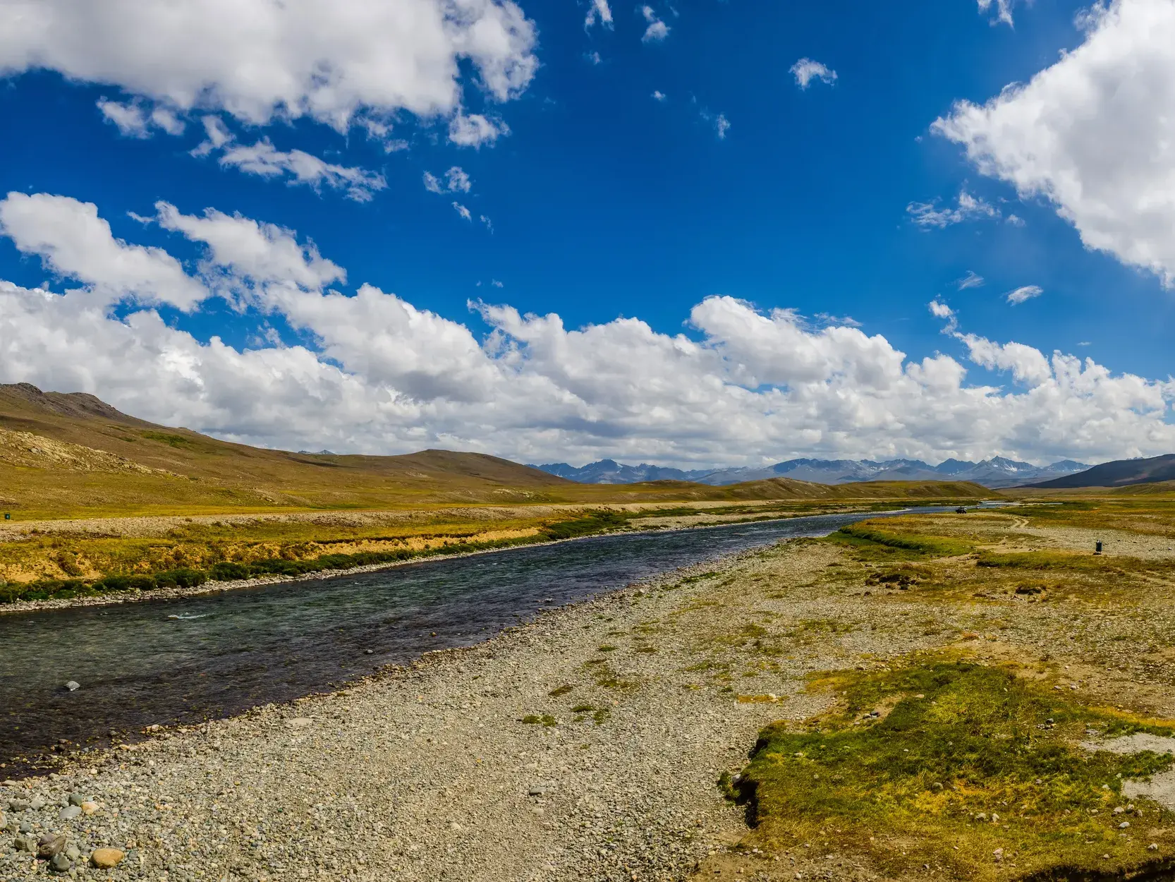 Weite Flusslandschaft auf der Hochebene des Deosai-Nationalparks in Pakistan mit Blick auf die fernen Gebirgsketten.