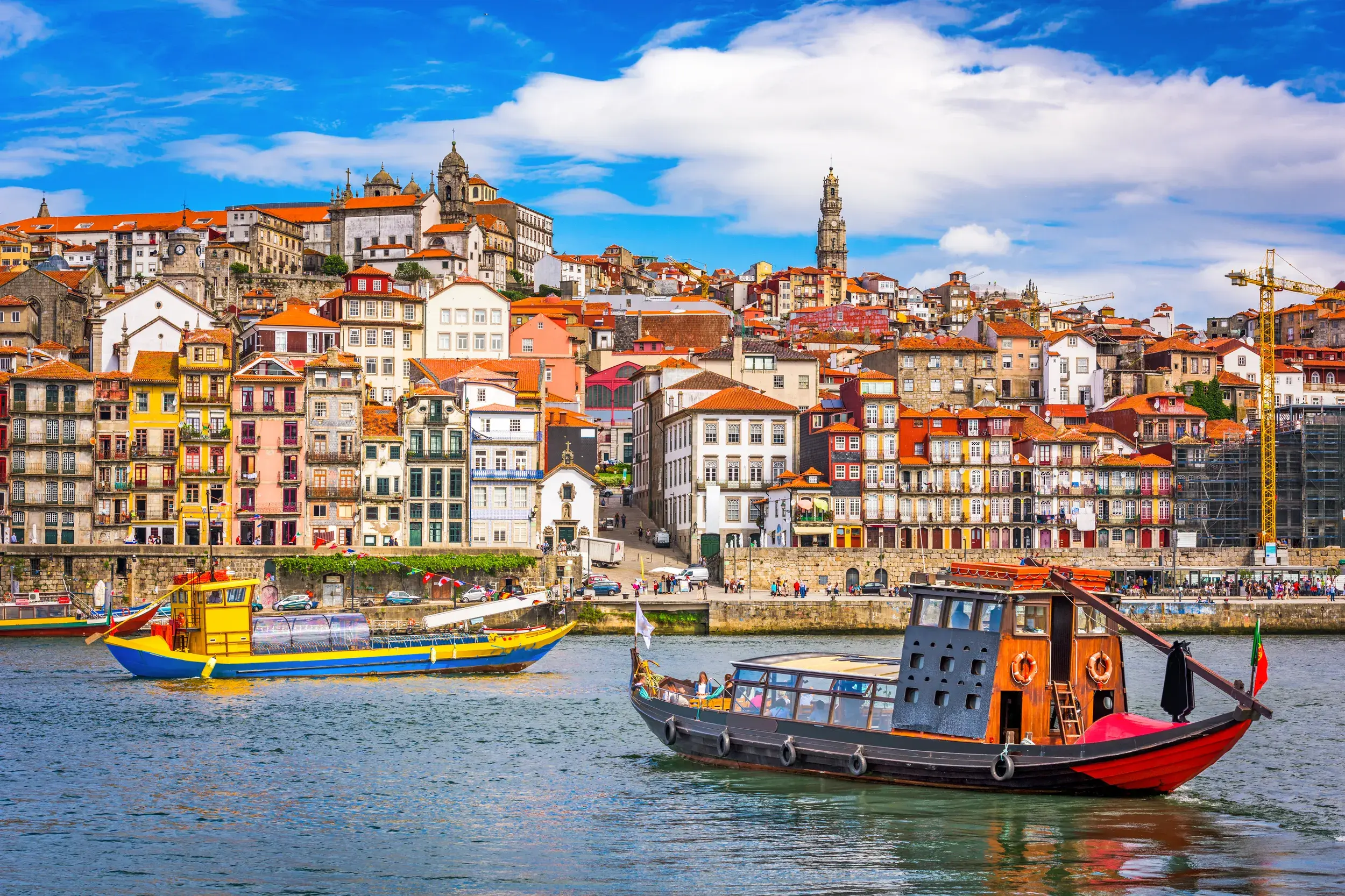 Traditionelle Boote auf dem Fluss vor der sonnigen Hügellandschaft des bunten UNESCO-Welterbes Ribeira in Porto.