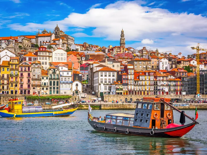 Traditionelle Boote auf dem Fluss vor der sonnigen Hügellandschaft des bunten UNESCO-Welterbes Ribeira in Porto.