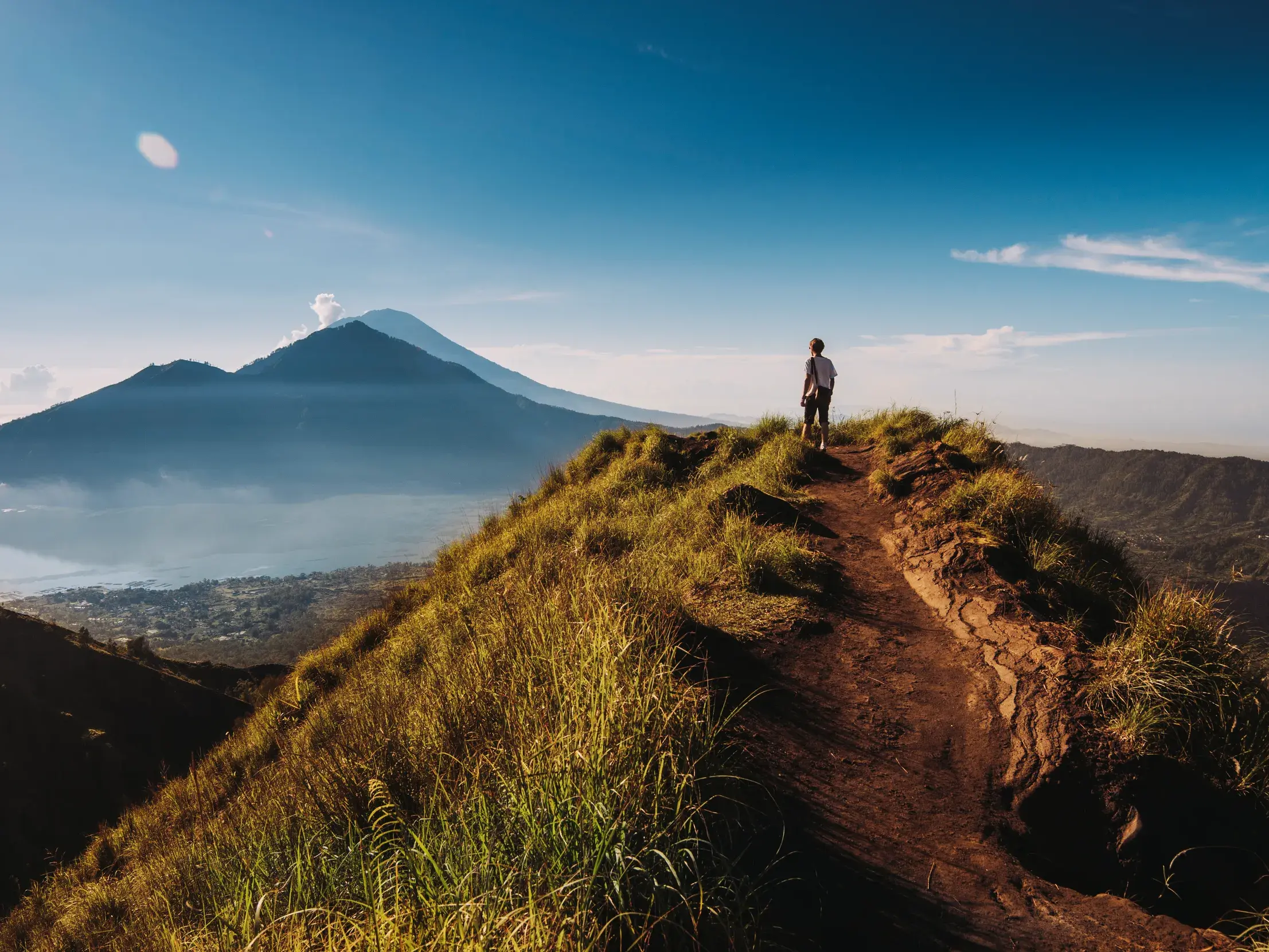 Auf einer geführten Rundreise durch Bali: Ein Reisender blickt am Morgen vom Kraterrand auf den Vulkan Batur und den Batursee.