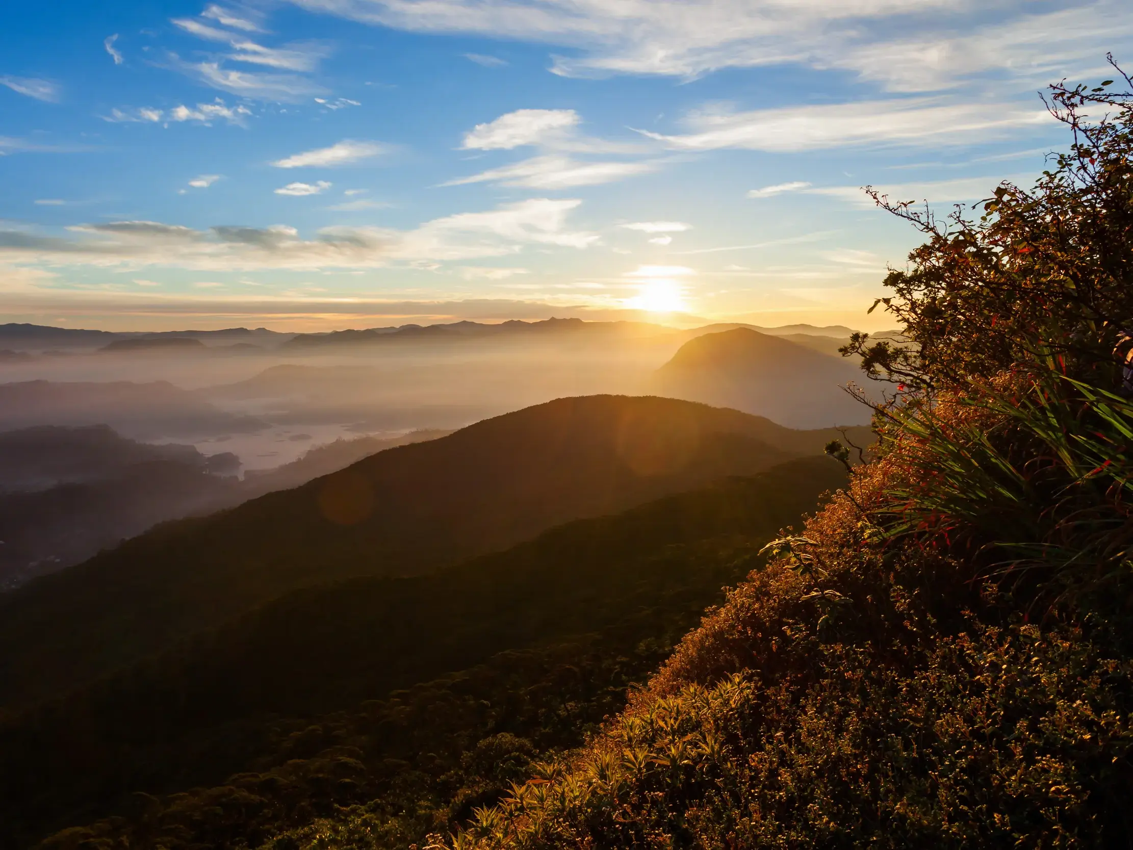 Magischer Sonnenaufgang auf dem Gipfel des Adam's Peak mit Blick über die nebelverhangenen Täler und Berge Sri Lankas.