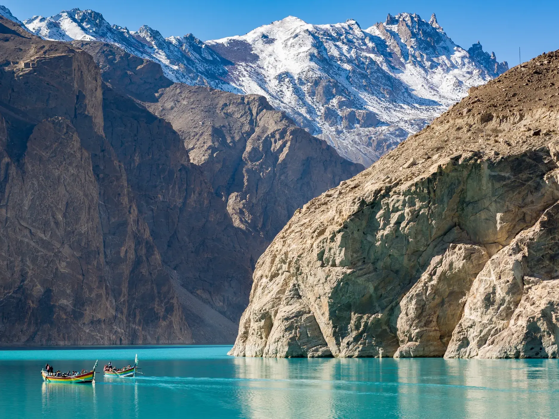 Zwei Boote mit Reisenden auf dem leuchtend türkisen Attabad-See, umgeben von steilen Felswänden des Karakorum in Pakistan.