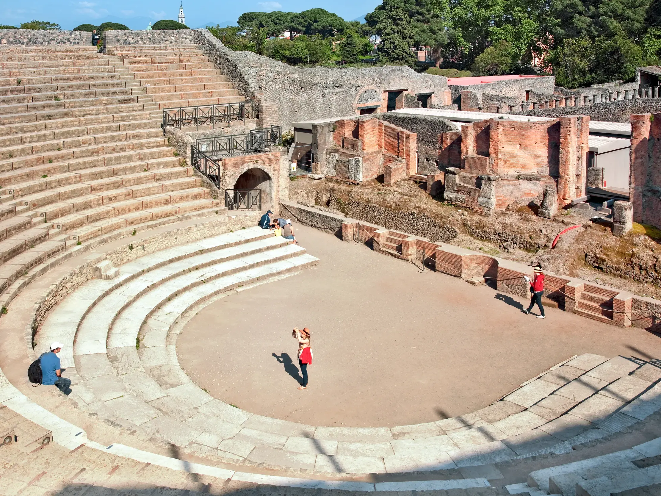 Weitläufige Ansicht des antiken Theaters in Pompeji mit seinen Steinstufen, wo Touristen die archäologische Stätte erkunden.