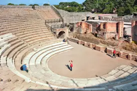 Weitläufige Ansicht des antiken Theaters in Pompeji mit seinen Steinstufen, wo Touristen die archäologische Stätte erkunden.
