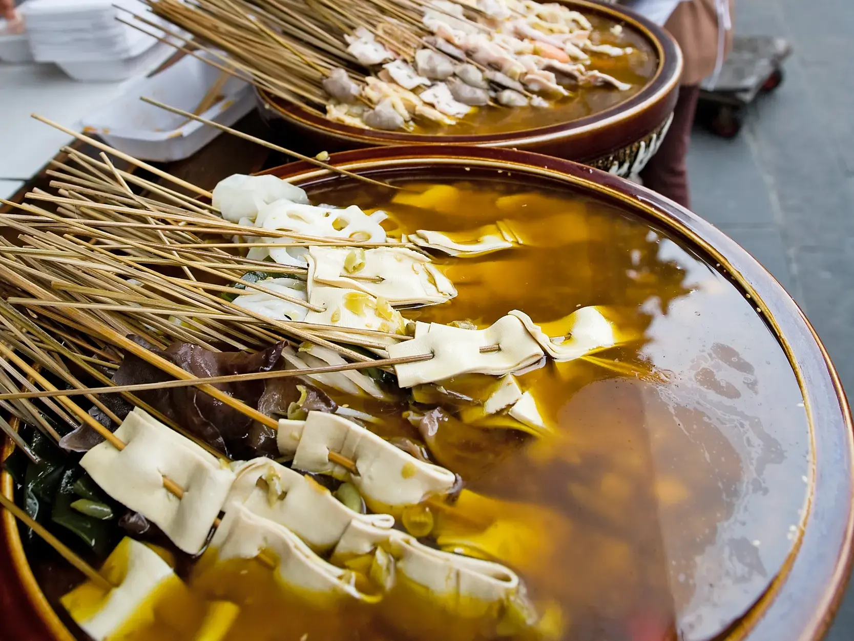 Nahaufnahme von chinesischen Streetfood-Spießen mit Tofu und Gemüse in einer würzigen Brühe während einer Hutong-Tour in Beijing.
