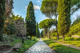 Wanderweg auf der alten Römerstraße Via Appia Antica bei Rom, gesäumt von hohen Zypressen, Pinien und antiken Ruinen.