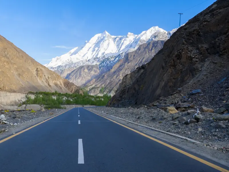 Der Karakorum Highway in Pakistan, gesäumt von kargen Felswänden, mit Blick auf den schneebedeckten Nanga Parbat.