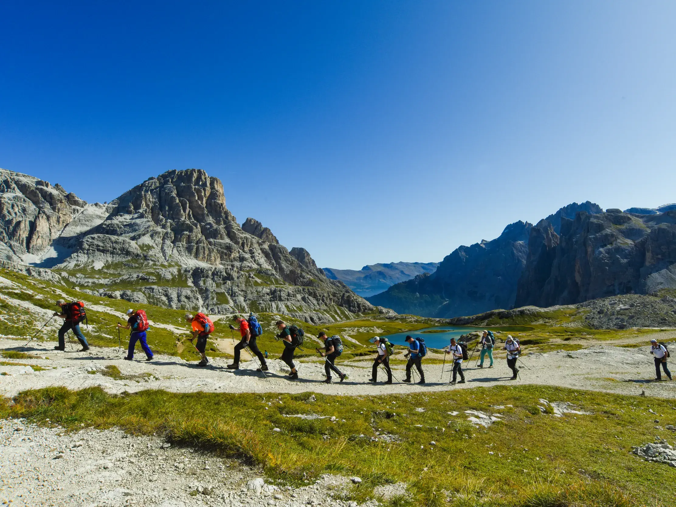 Reisegruppe auf einer Alpenüberquerung im Naturpark Drei Zinnen, wandert auf einem Weg entlang der markanten Felsformationen der Dolomiten.