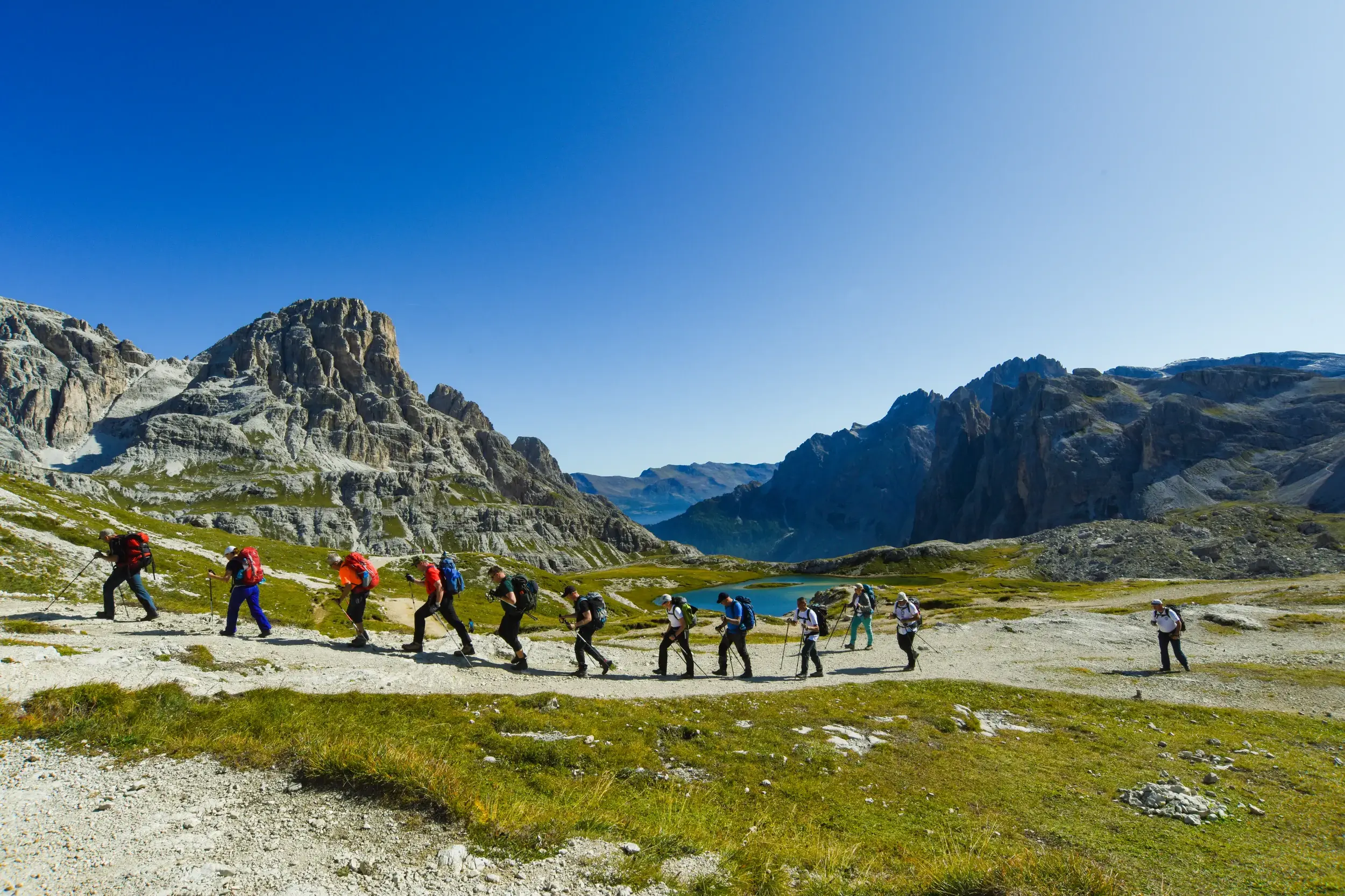 Reisegruppe auf einer Alpenüberquerung im Naturpark Drei Zinnen, wandert auf einem Weg entlang der markanten Felsformationen der Dolomiten.
