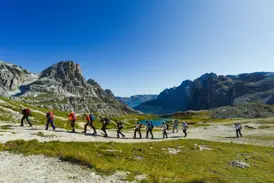 Reisegruppe auf einer Alpenüberquerung im Naturpark Drei Zinnen, wandert auf einem Weg entlang der markanten Felsformationen der Dolomiten.