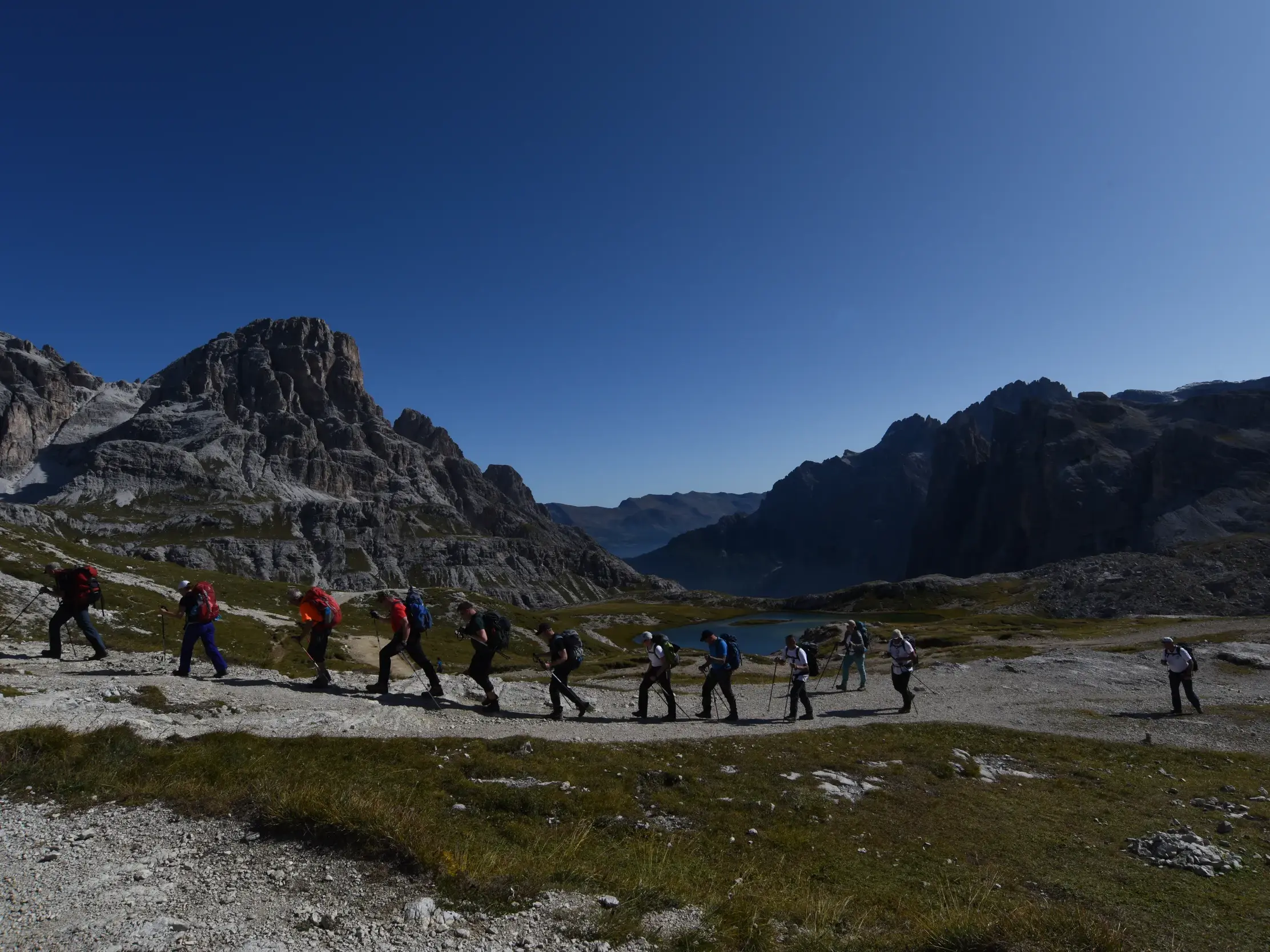 Eine Hauser-Wandergruppe beim Trekking auf einem Pfad vor der Felskulisse der Drei Zinnen im UNESCO Welterbe Dolomiten.