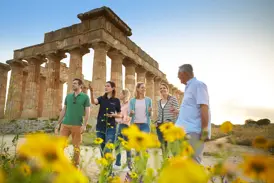 Eine Studiosus-Reiseleiterin erklärt einer kleinen Gruppe auf einer Studienreise die von Wildblumen umgebenen Tempelruinen von Selinunt.