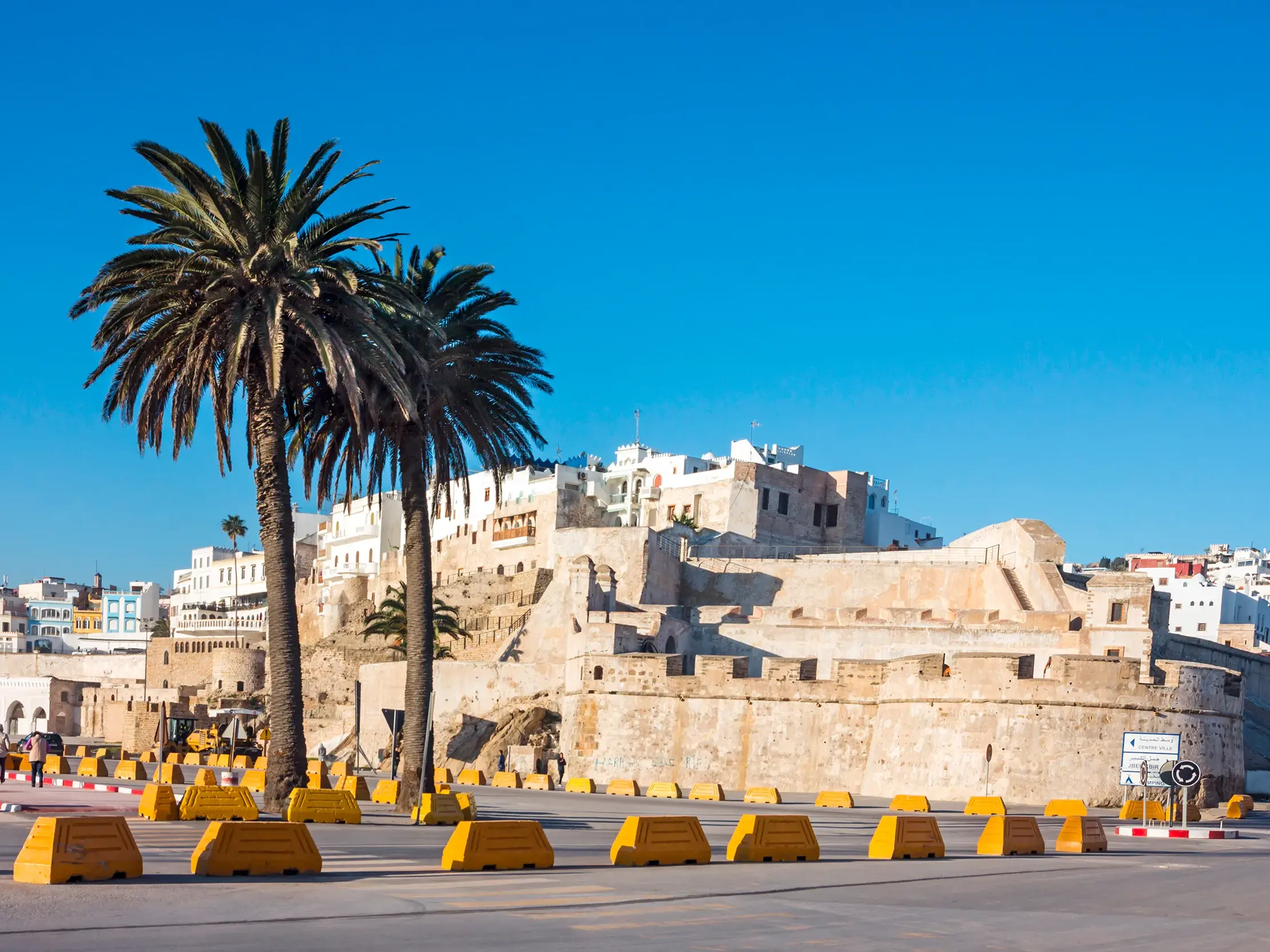 Sonnige Ansicht der historischen Kasbah von Tanger mit ihren Festungsmauern, der Medina und hohen Palmen im Vordergrund.