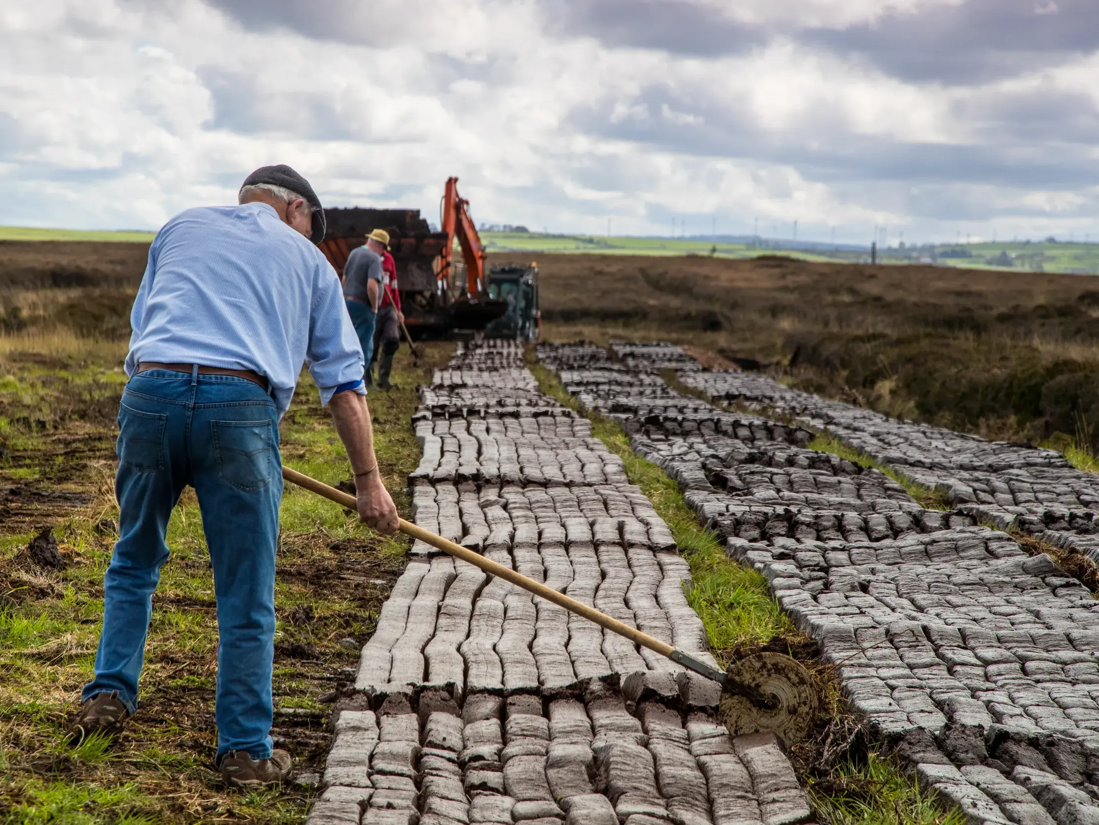 Ein traditioneller Torfstecher wendet von Hand Torfsoden zum Trocknen in der weiten Moorlandschaft von Connemara, Irland.