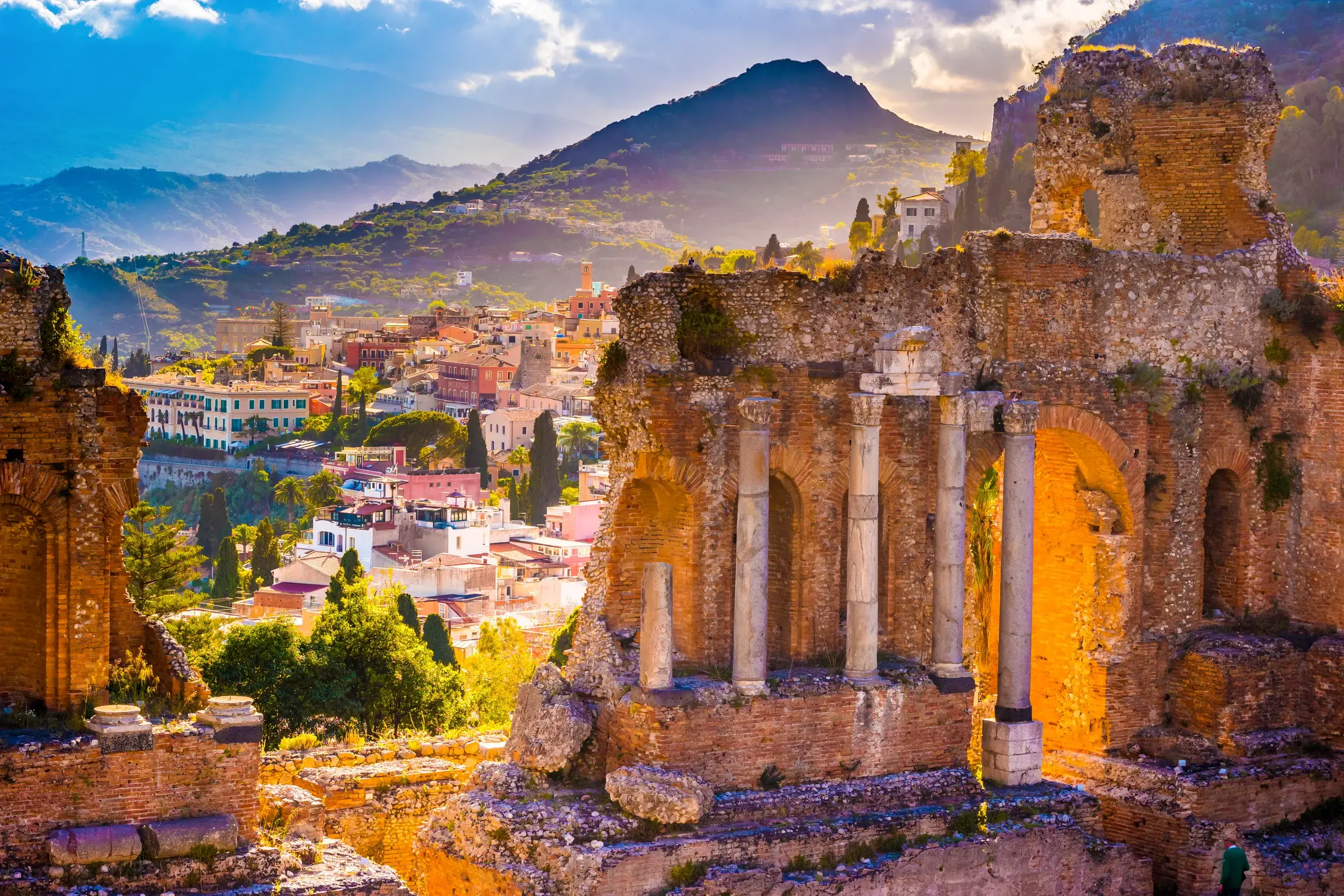 Die antiken Ruinen des Theaters von Taormina im warmen Abendlicht, mit malerischem Blick auf die Stadt und die Berge Siziliens.
