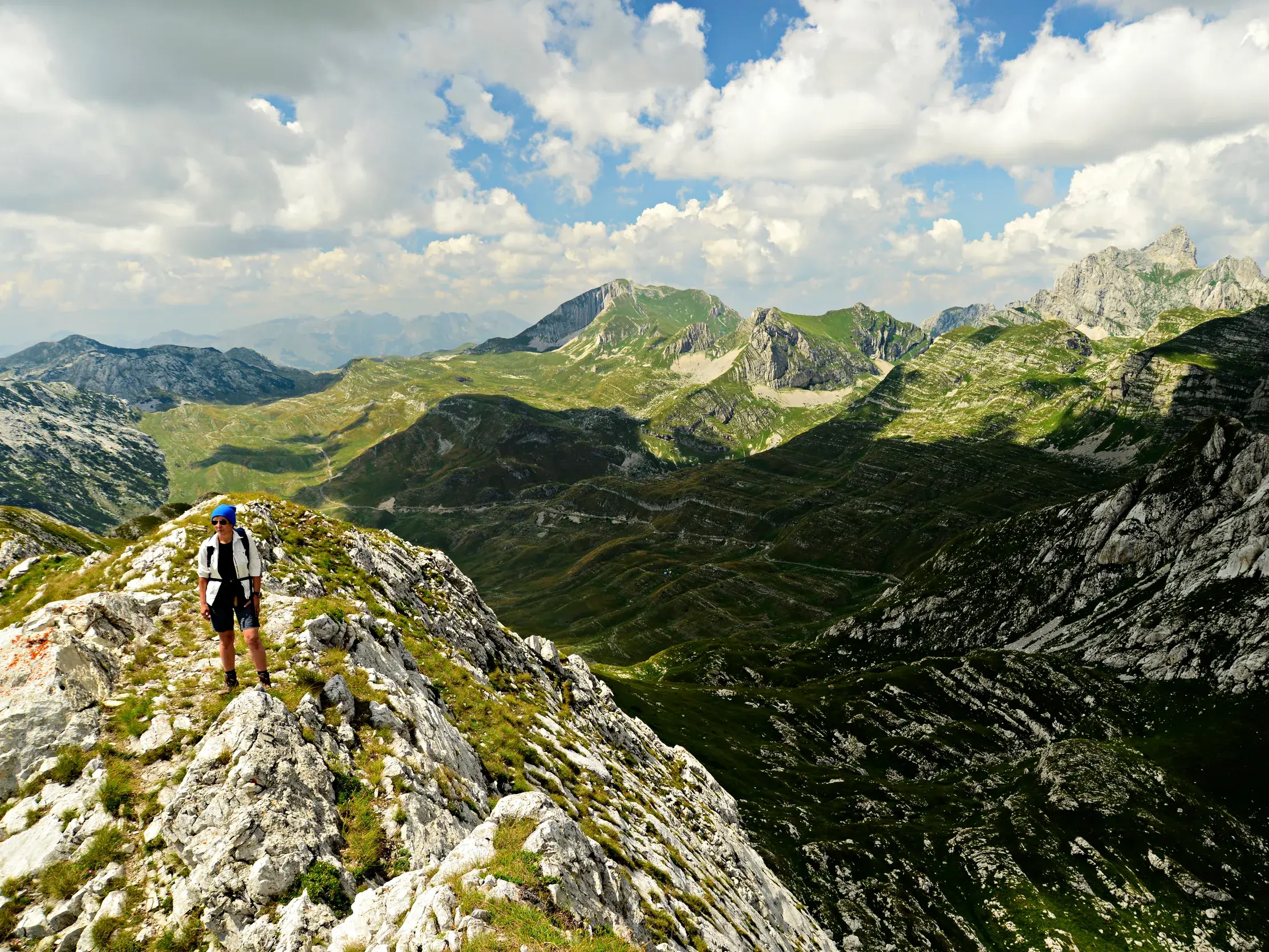 Wanderin auf dem schmalen Gipfelgrat der Crvena Greda mit weitem Blick über die grünen Täler des Durmitor Nationalparks.