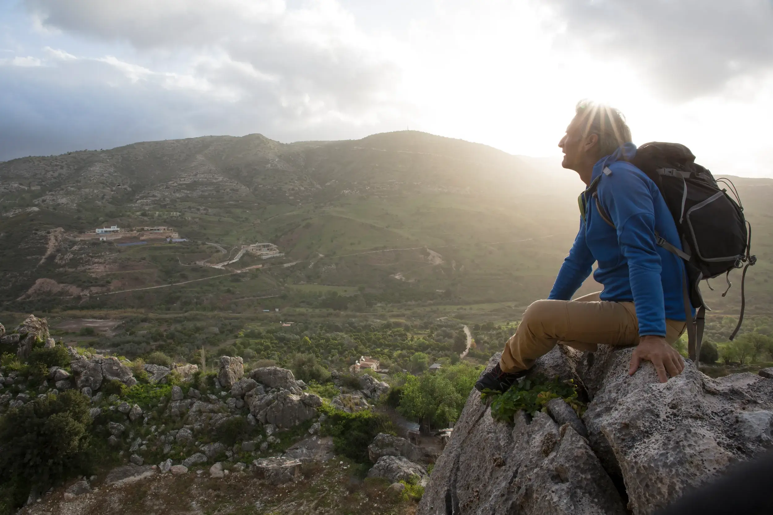Ein Wanderer macht bei Sonnenuntergang eine Pause auf einem Felsen und genießt die weite Aussicht über das Troodosgebirge auf Zypern.