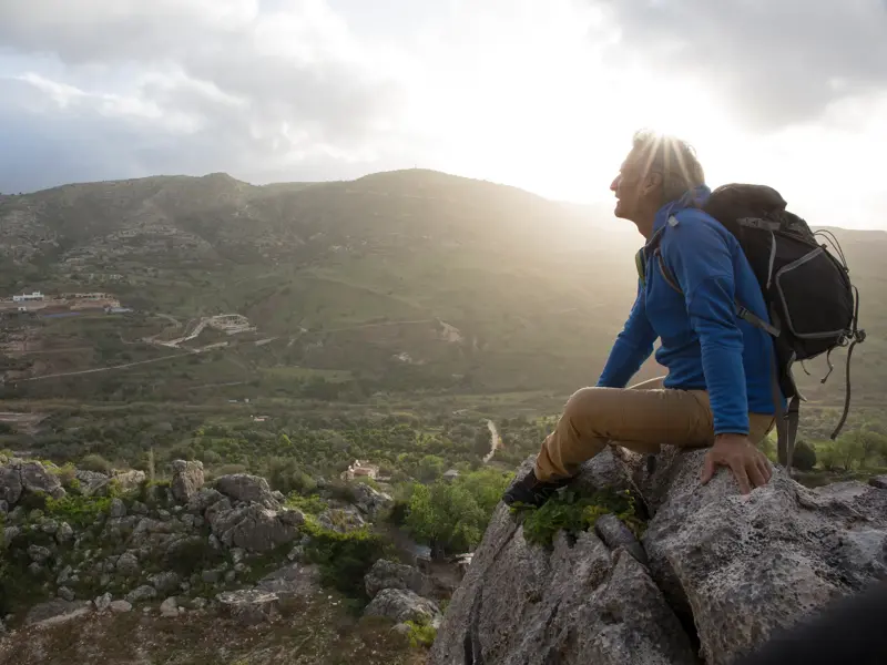 Ein Wanderer macht bei Sonnenuntergang eine Pause auf einem Felsen und genießt die weite Aussicht über das Troodosgebirge auf Zypern.