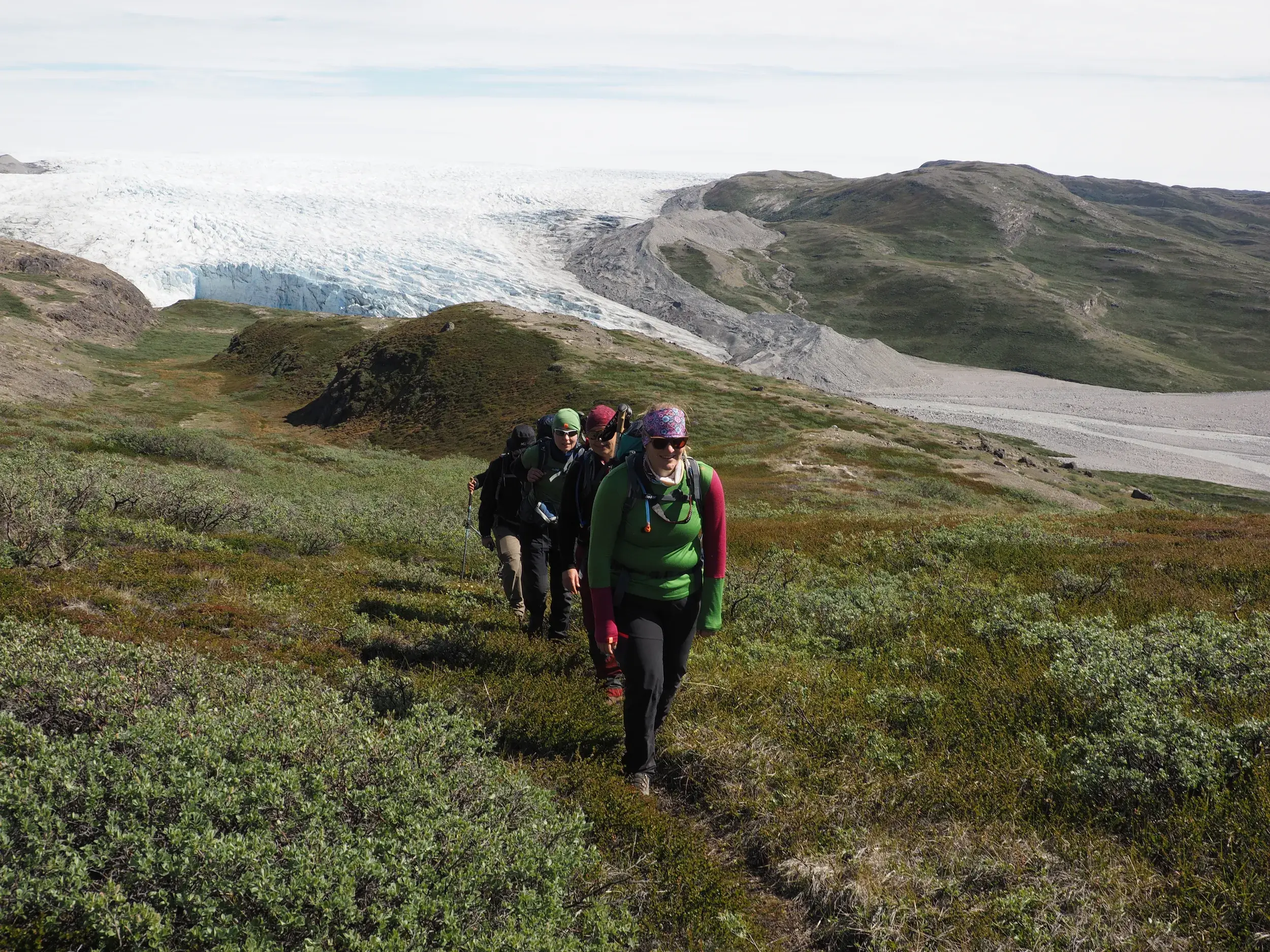 Eine Wandergruppe auf Trekking-Tour durch die grüne Tundra mit Blick auf die Abbruchkante des Russel-Gletschers in Grönland.