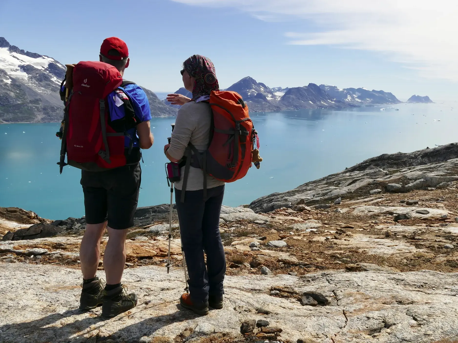 Zwei Trekking-Reisende genießen auf einer Wanderung in Ostgrönland den Ausblick auf einen Fjord mit Eisbergen.