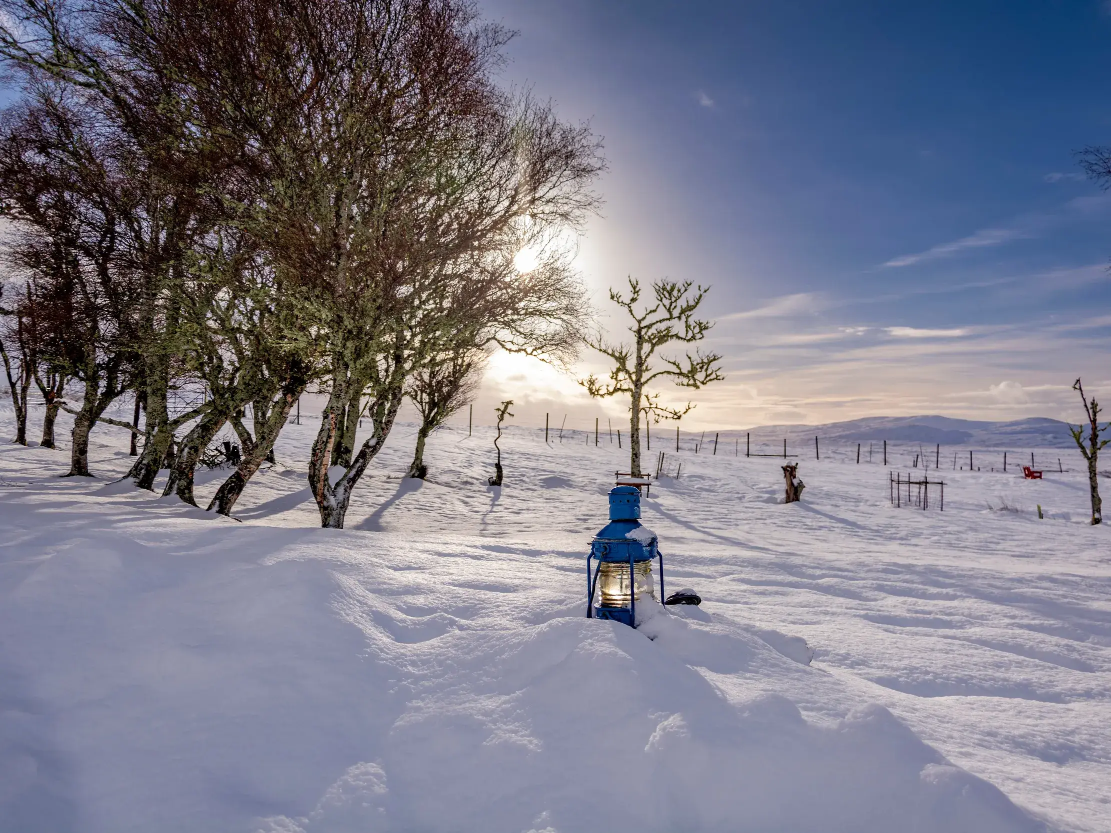Eine blaue Laterne leuchtet im tiefen Schnee. Im Hintergrund die weite, verschneite Landschaft der winterlichen Highlands.
