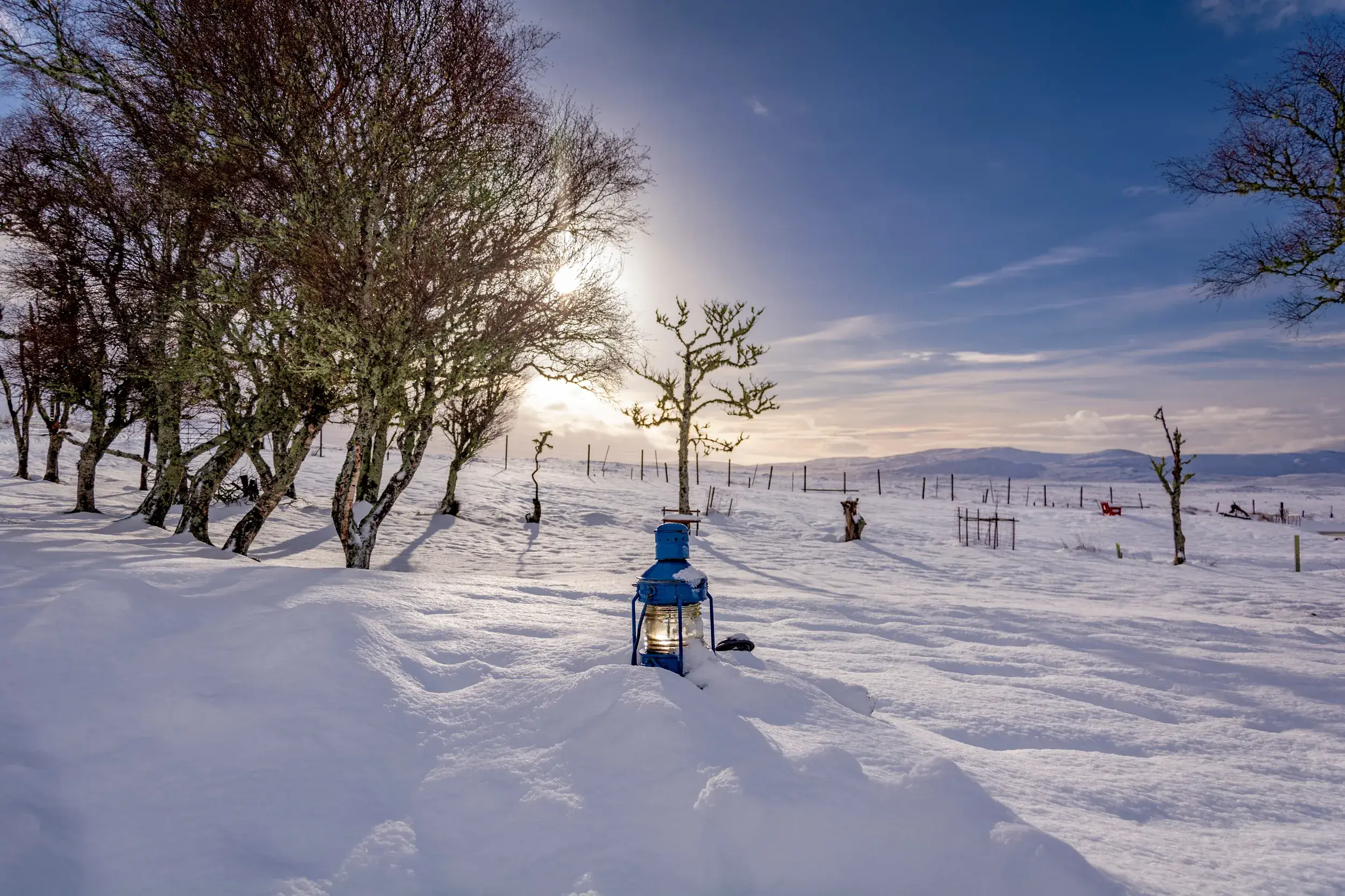 Eine blaue Laterne leuchtet im tiefen Schnee. Im Hintergrund die weite, verschneite Landschaft der winterlichen Highlands.
