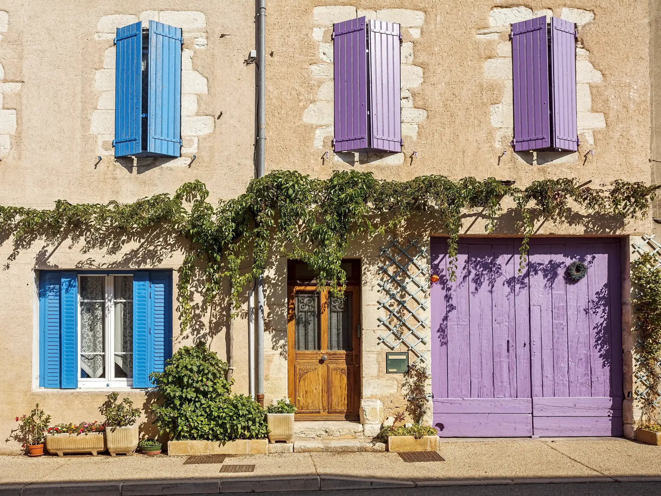 Typische Steinfassade in einem Dorf im Naturpark Luberon in der Provence mit blauen und lila Fensterläden und Efeubewuchs.