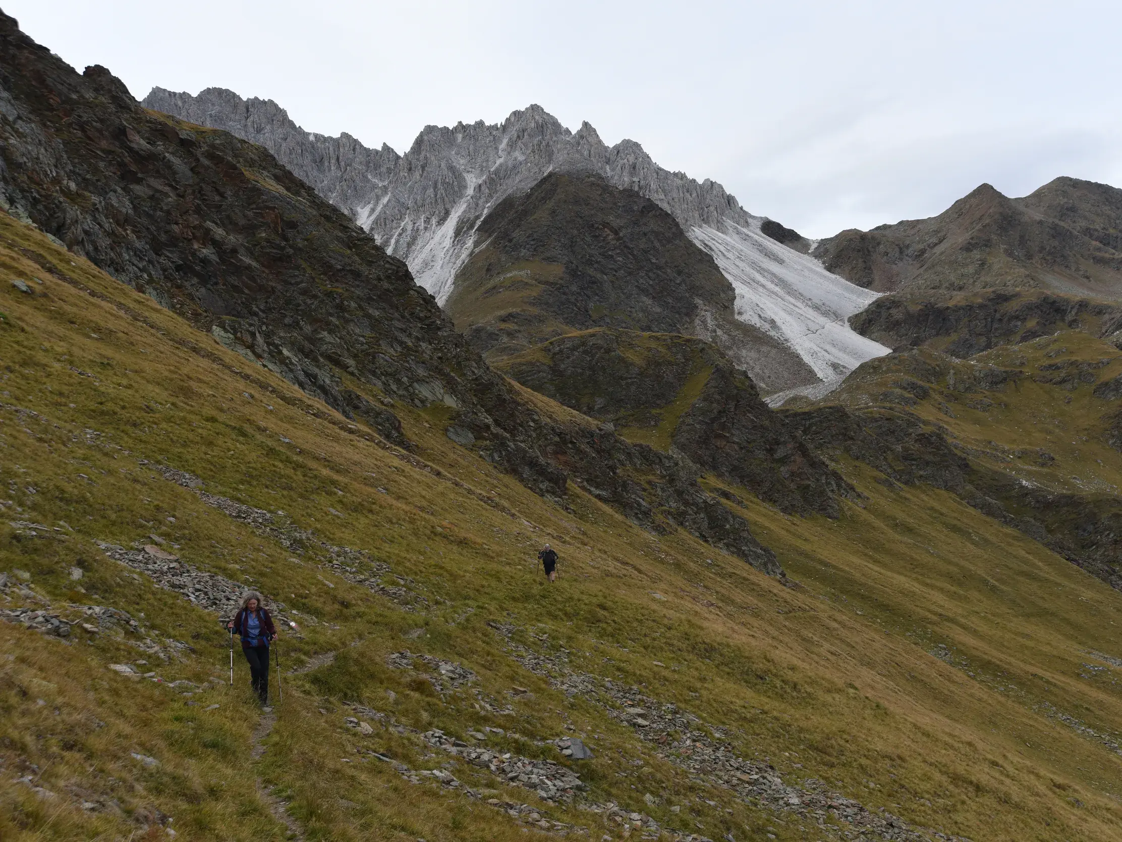 Zwei Wanderer mit Trekkingstöcken auf einem schmalen Pfad am Hang vor der Felskulisse der Tribulaune in den Stubaier Alpen.
