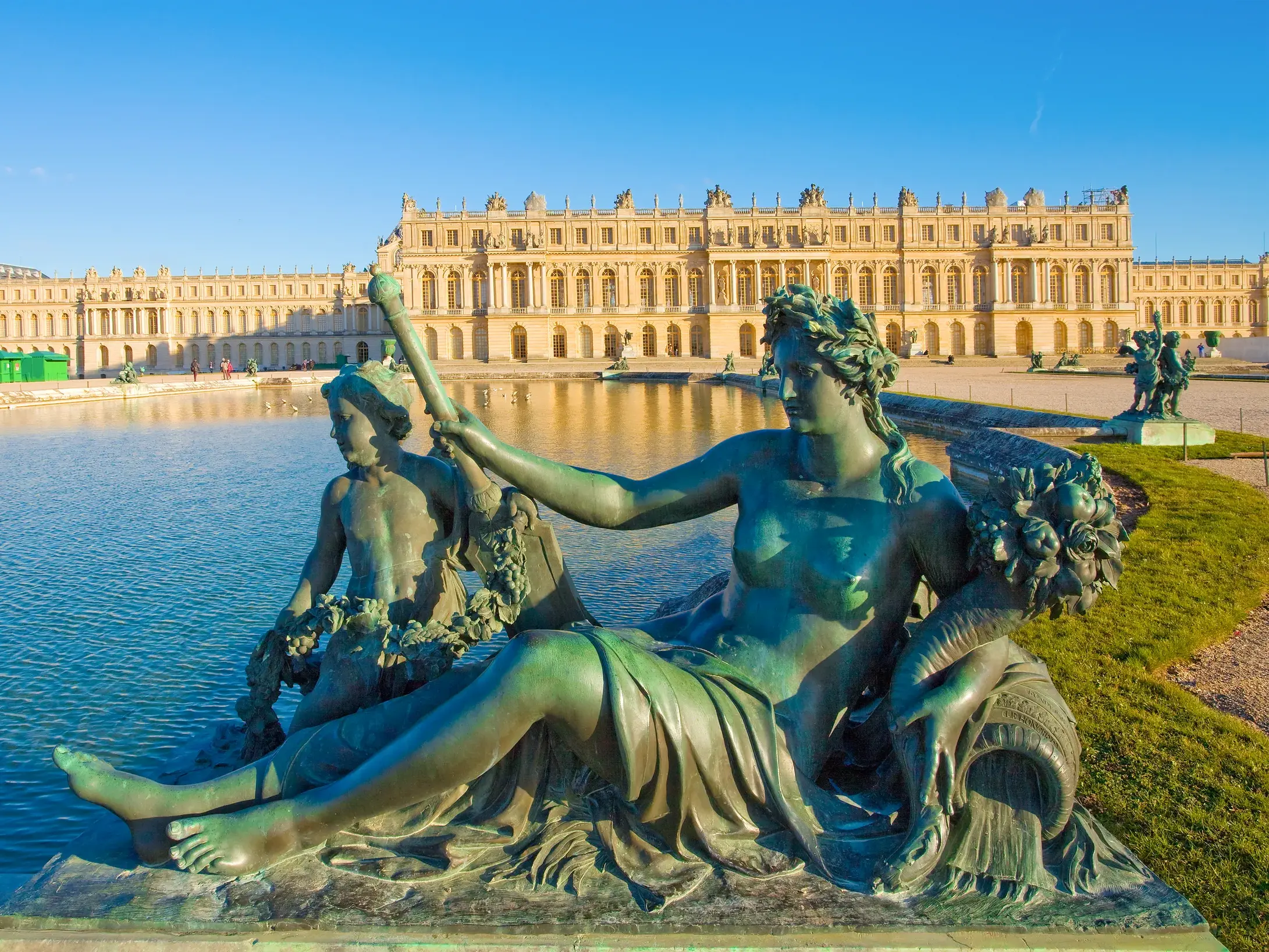 Prachtvolle Bronzestatue am Wasserbecken in den Parkanlagen vor der sonnenbeschienenen Fassade des Schlosses von Versailles.