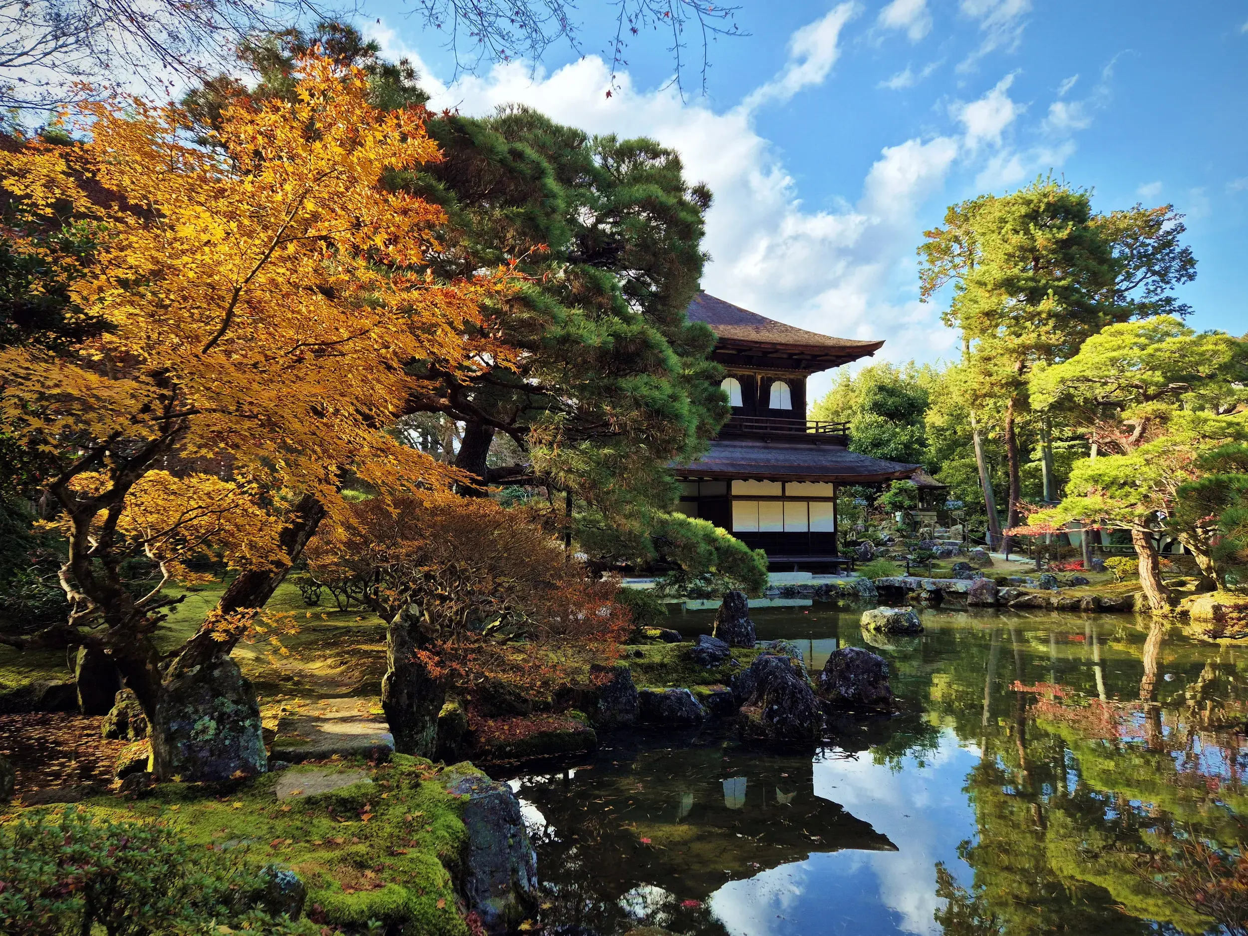 Der Silberne Pavillon Ginkaku-ji in Kyoto, umgeben von einem japanischen Garten mit leuchtendem Herbstlaub und Spiegelung im Teich.
