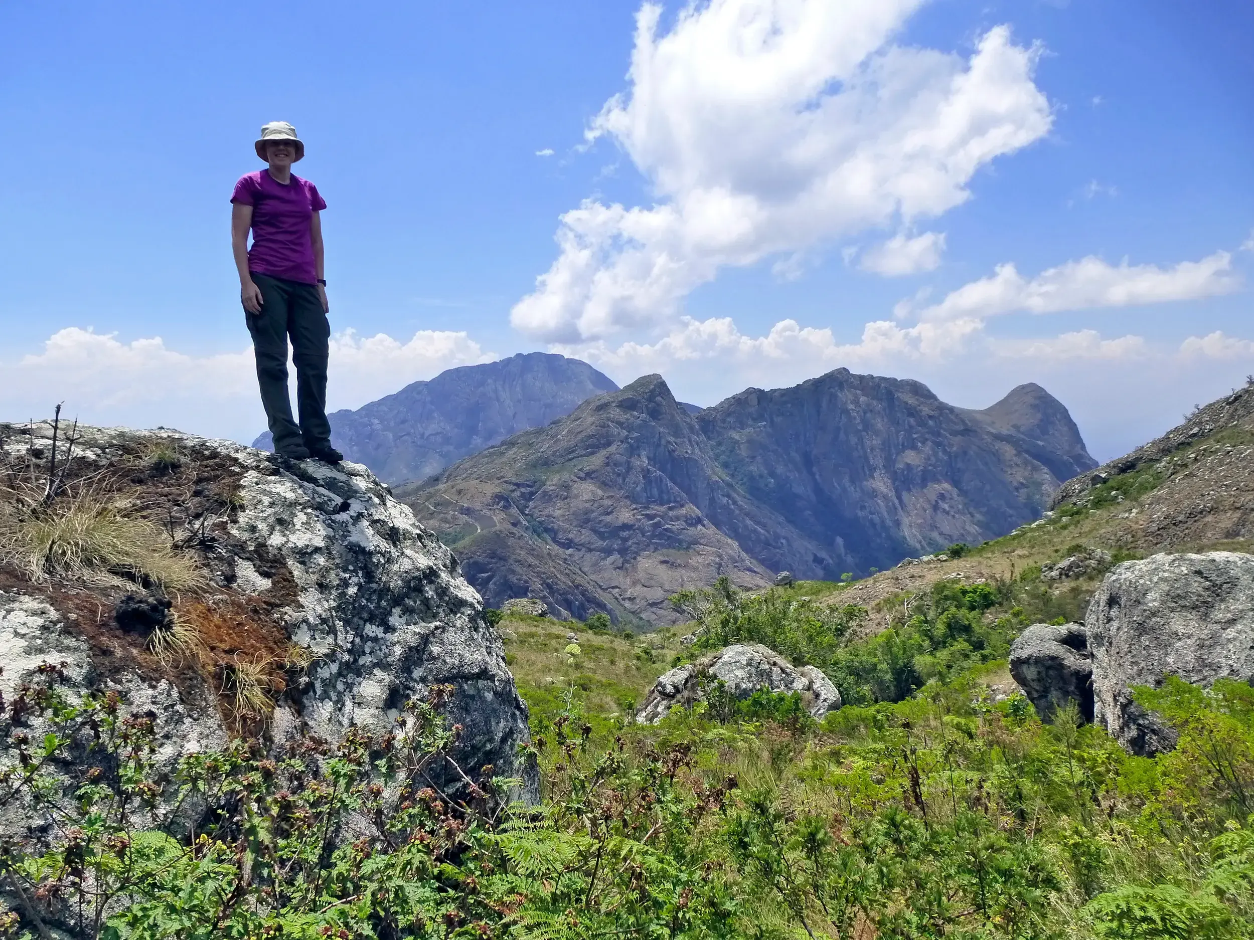 Wanderin steht auf einem Felsen und genießt den Panoramablick auf die imposanten Gipfel des Mulanje Bergmassivs in Malawi.