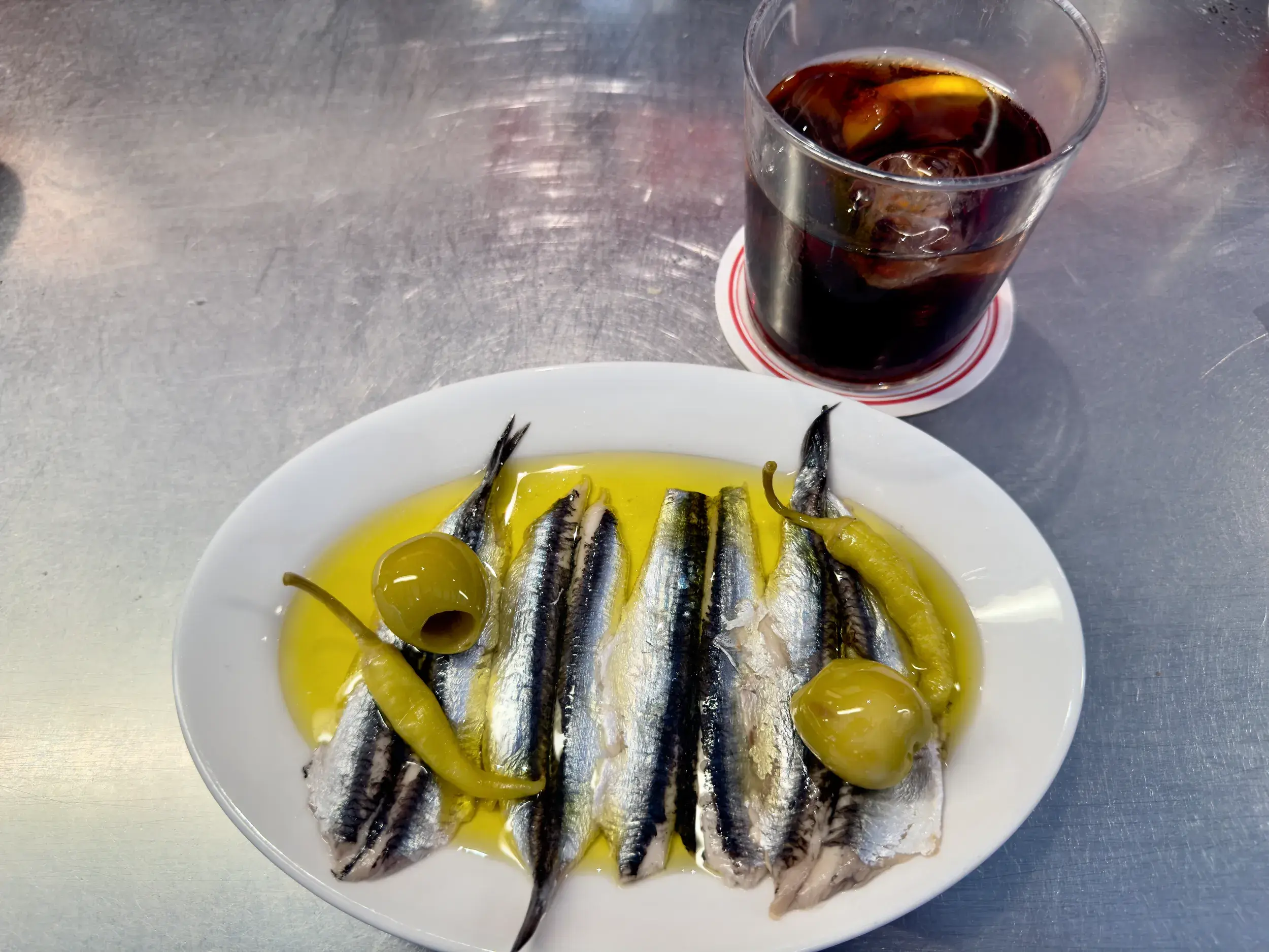 Typisch spanische Tapa auf einer Bar-Theke: Marinierte Sardellen in Olivenöl mit Oliven und Peperoni auf einem Teller.