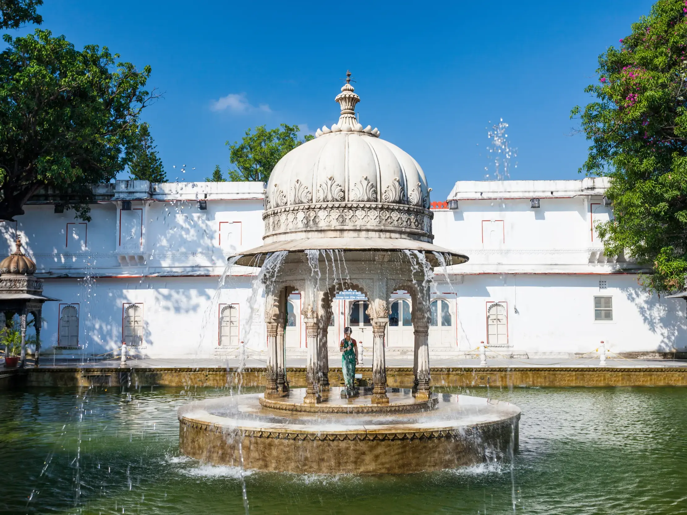 Prachtvoller Marmorbrunnen im Garten Sahelion-ki Bari in Udaipur, umgeben von einem Wasserbecken und grünen Bäumen.