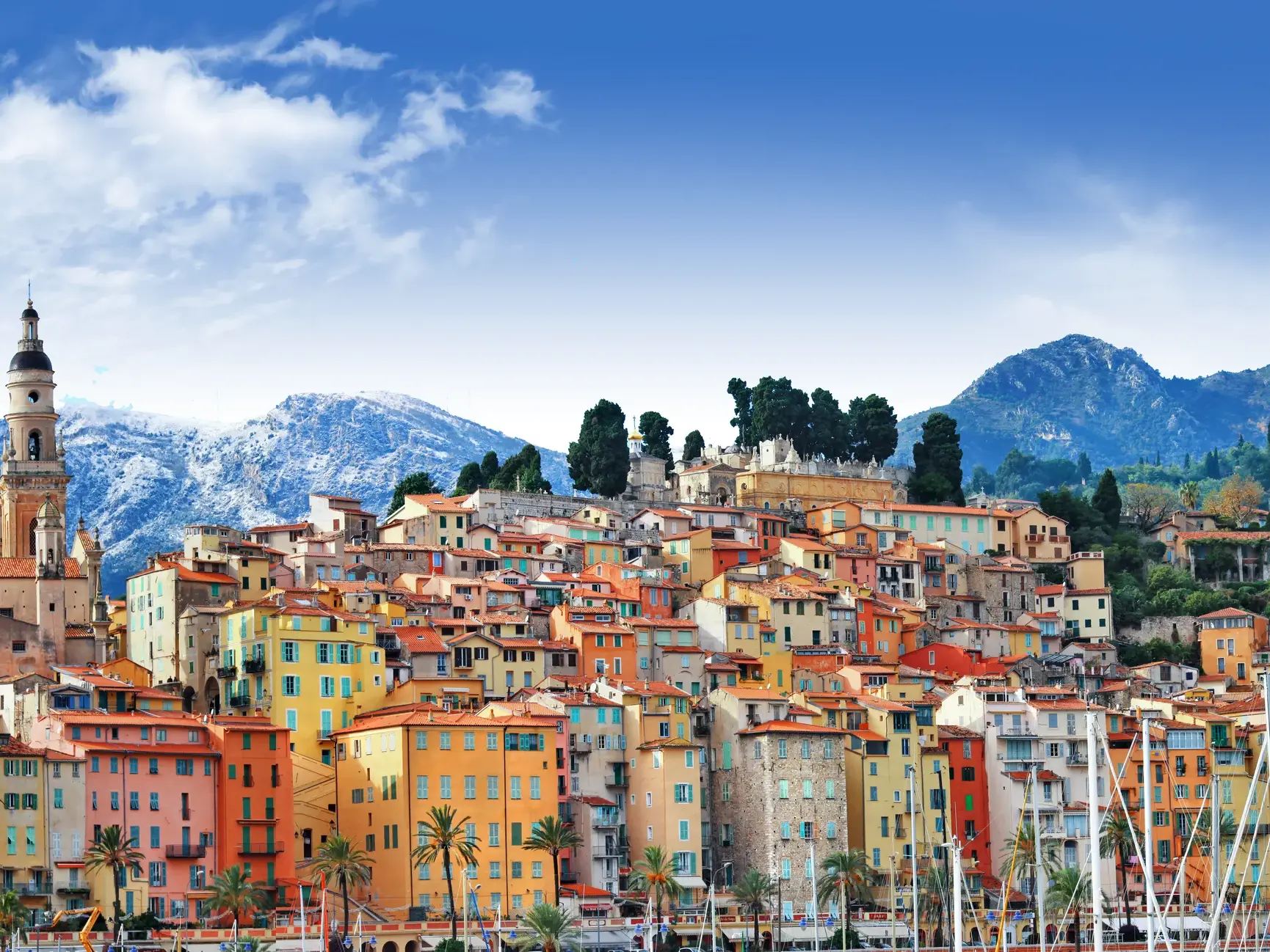 Die farbenfrohen Häuser der Altstadt von Menton an der Côte d'Azur mit den schneebedeckten Alpen im Hintergrund.