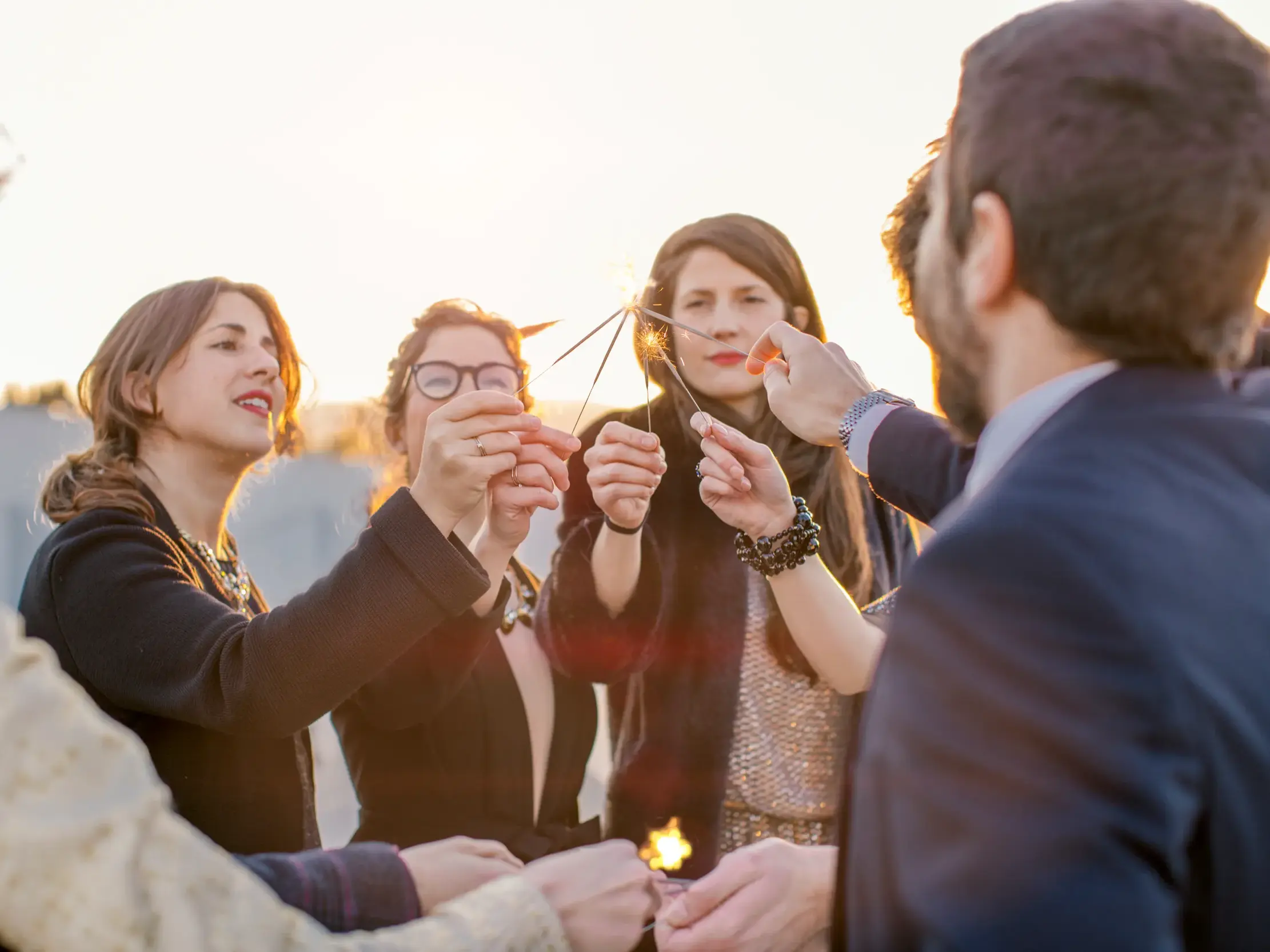 Eine Gruppe Alleinreisender feiert auf einer Singlereise in Madrid bei Sonnenuntergang mit Wunderkerzen den Jahreswechsel.