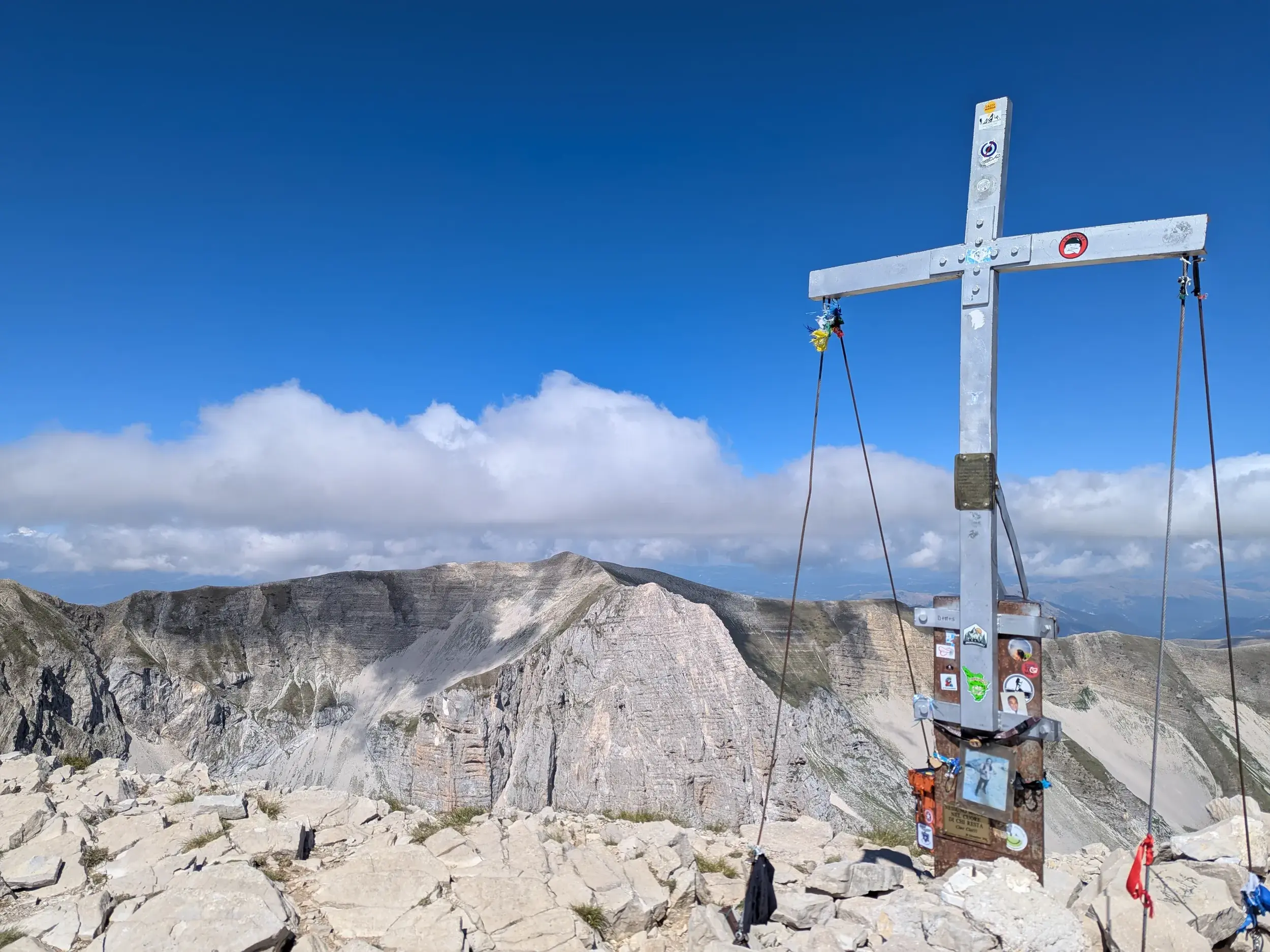 Gipfelkreuz auf dem Monte Vettore mit Panoramablick über die felsige Berglandschaft des Nationalparks Monti Sibillini.