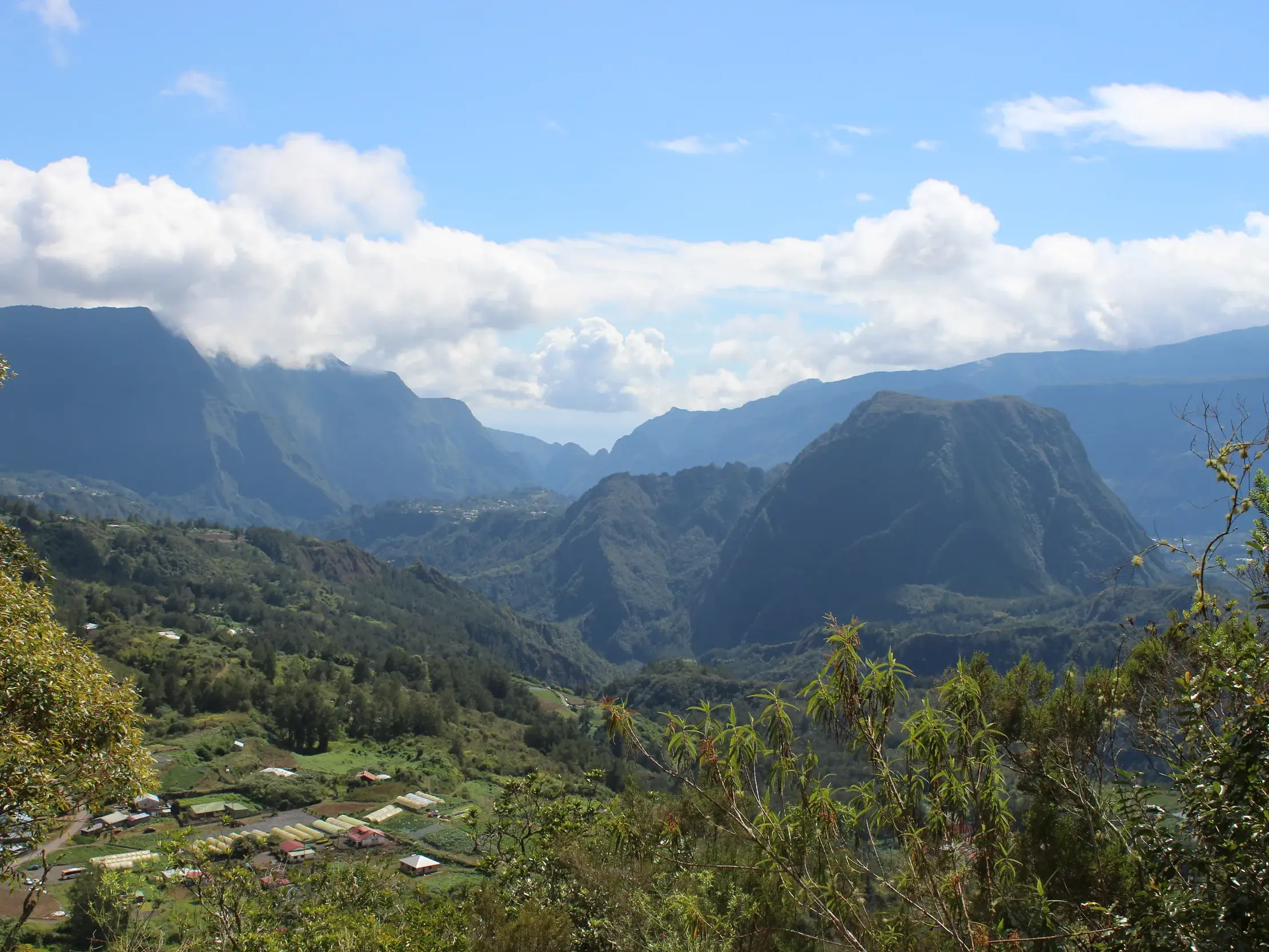 Weitblick über die üppig grüne Berglandschaft des Cirque de Salazie auf La Réunion mit einem kleinen Dorf im Talkessel.