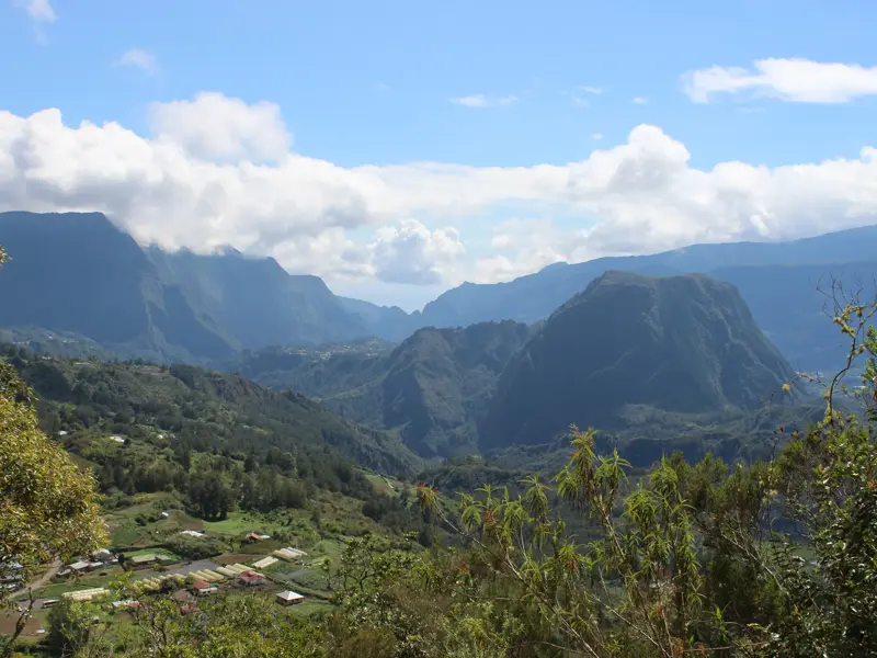 Weitblick über die üppig grüne Berglandschaft des Cirque de Salazie auf La Réunion mit einem kleinen Dorf im Talkessel.