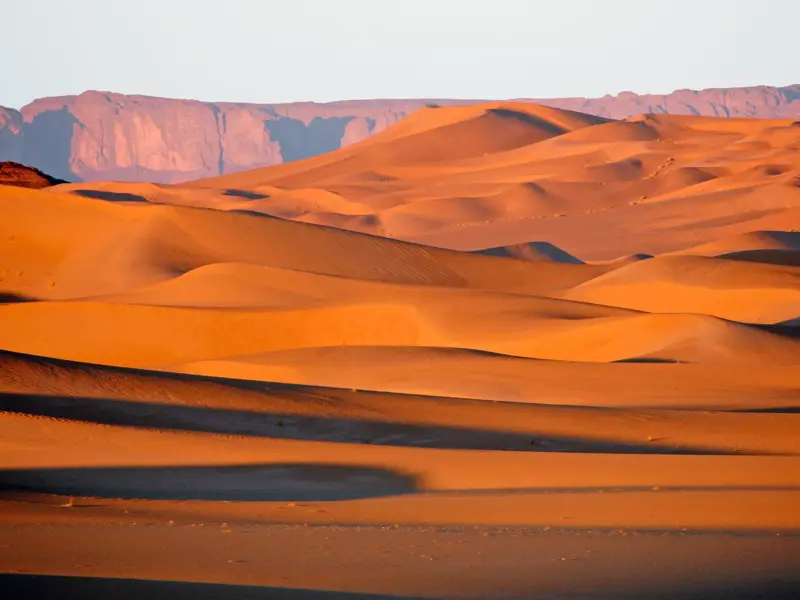 Goldene Dünen des Erg d'Admer in Algerien, im Hintergrund das Tassili-Gebirge im sanften Licht der Abendsonne.