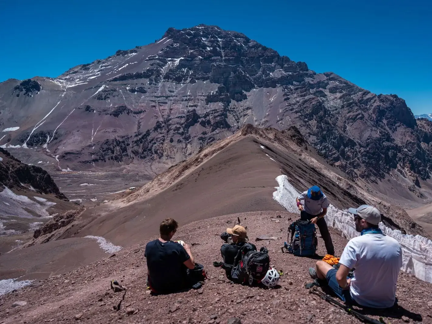 Vier Trekker pausieren auf dem Grat des Cerro Bonete mit beeindruckendem Blick auf die felsige Westwand des Aconcagua in den Anden.