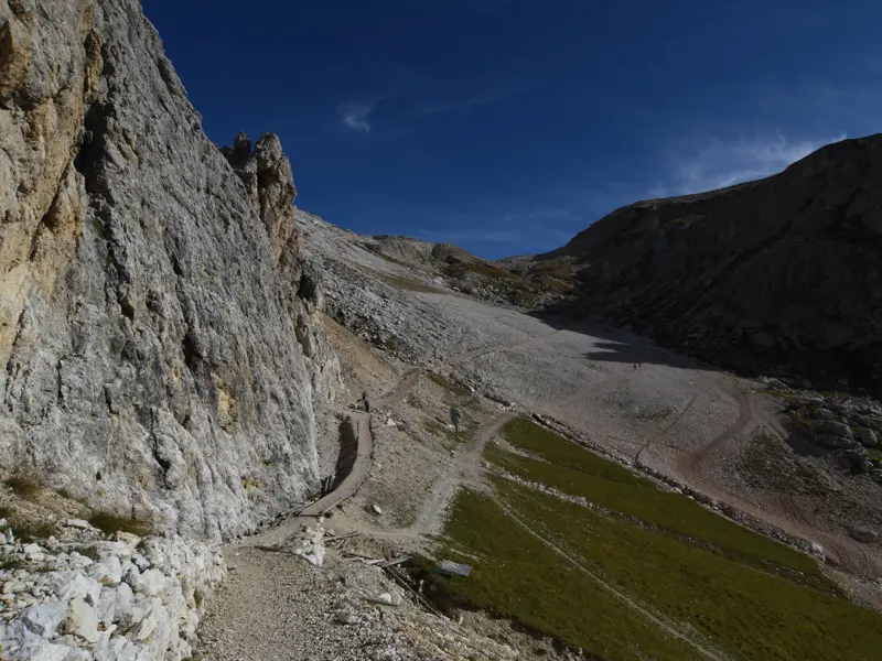 Wanderer auf einem schmalen Pfad an einer imposanten Felswand beim Trekking auf dem Höhenweg Alta Via 1 in den Dolomiten.