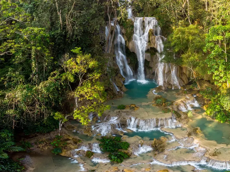 Die berühmten Kuang Sy Wasserfälle bei Luang Prabang stürzen über Kalksteinterrassen in türkise Becken im laotischen Dschungel.