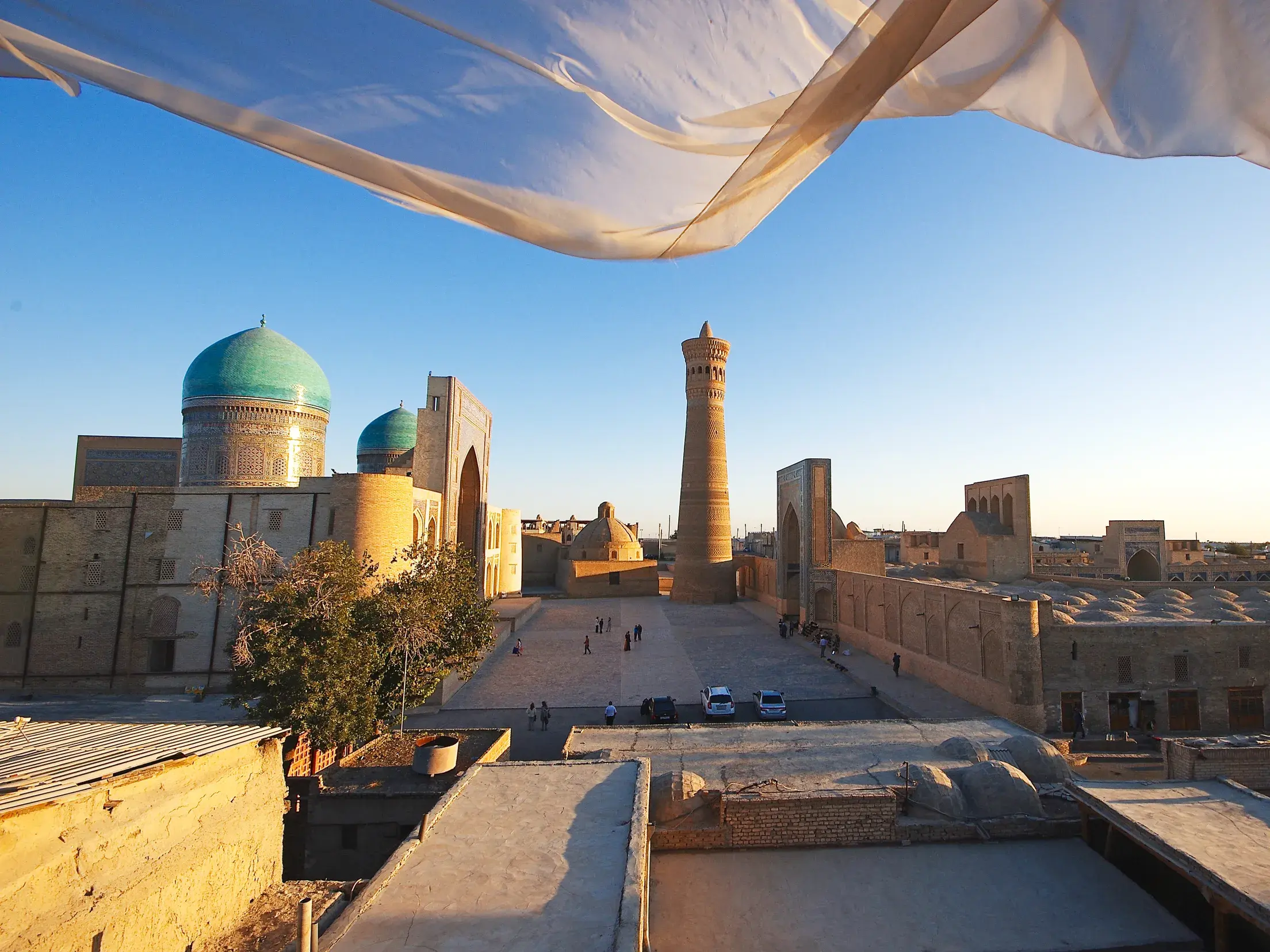 Ein wehender Schal rahmt den Blick auf das Kalon-Minarett und die türkisen Kuppeln der Mir-i-Arab-Madrasa in Buchara.