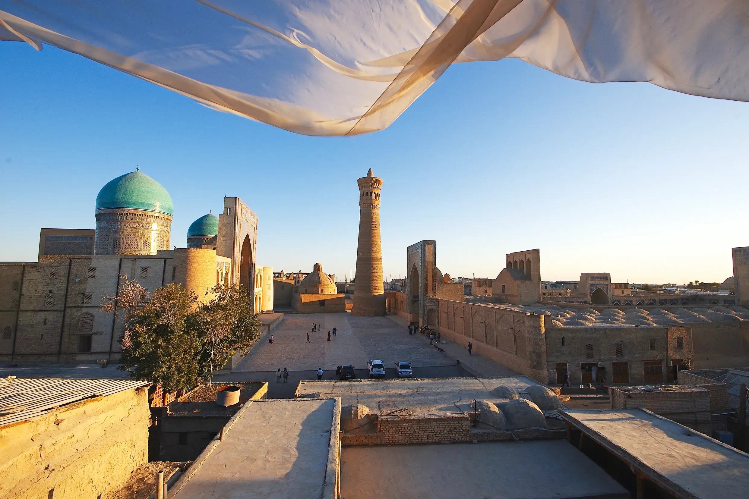 Ein wehender Schal rahmt den Blick auf das Kalon-Minarett und die türkisen Kuppeln der Mir-i-Arab-Madrasa in Buchara.